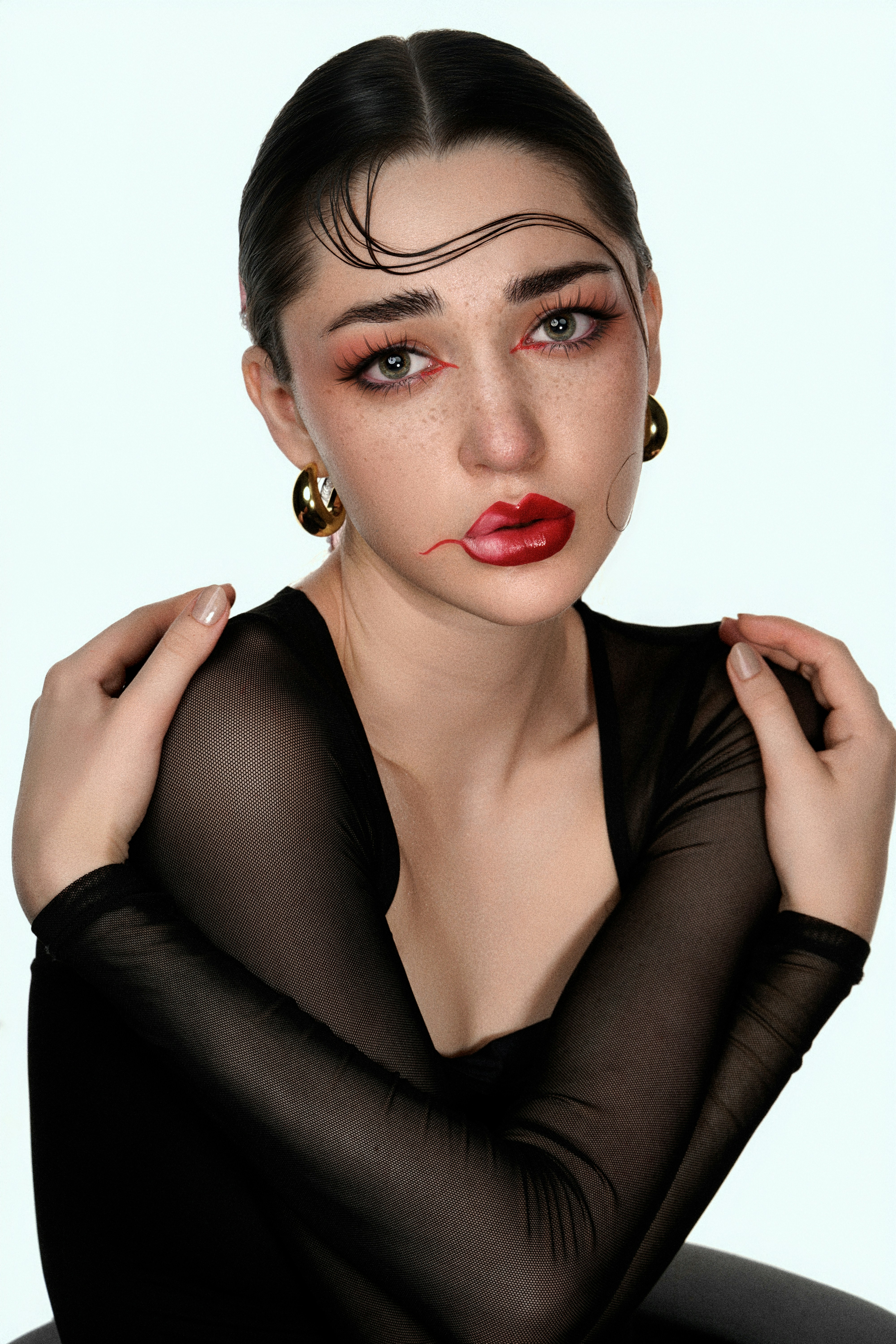 Woman with dramatic makeup and slicked hair poses.