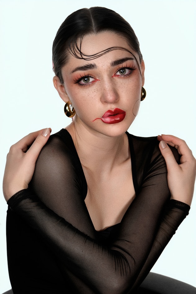 Woman with dramatic makeup and slicked hair poses.