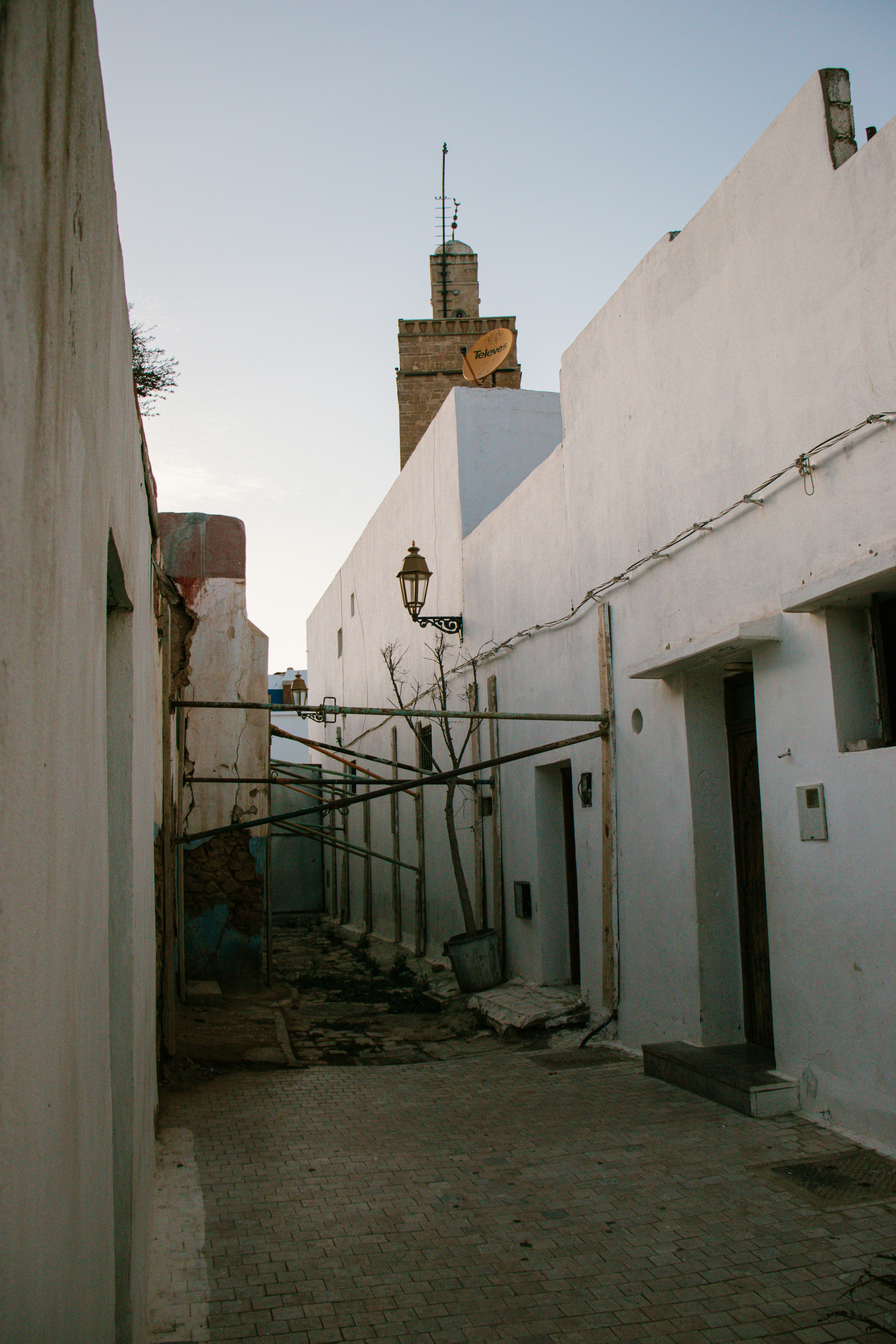 Narrow alleyway with white buildings and a distant tower.