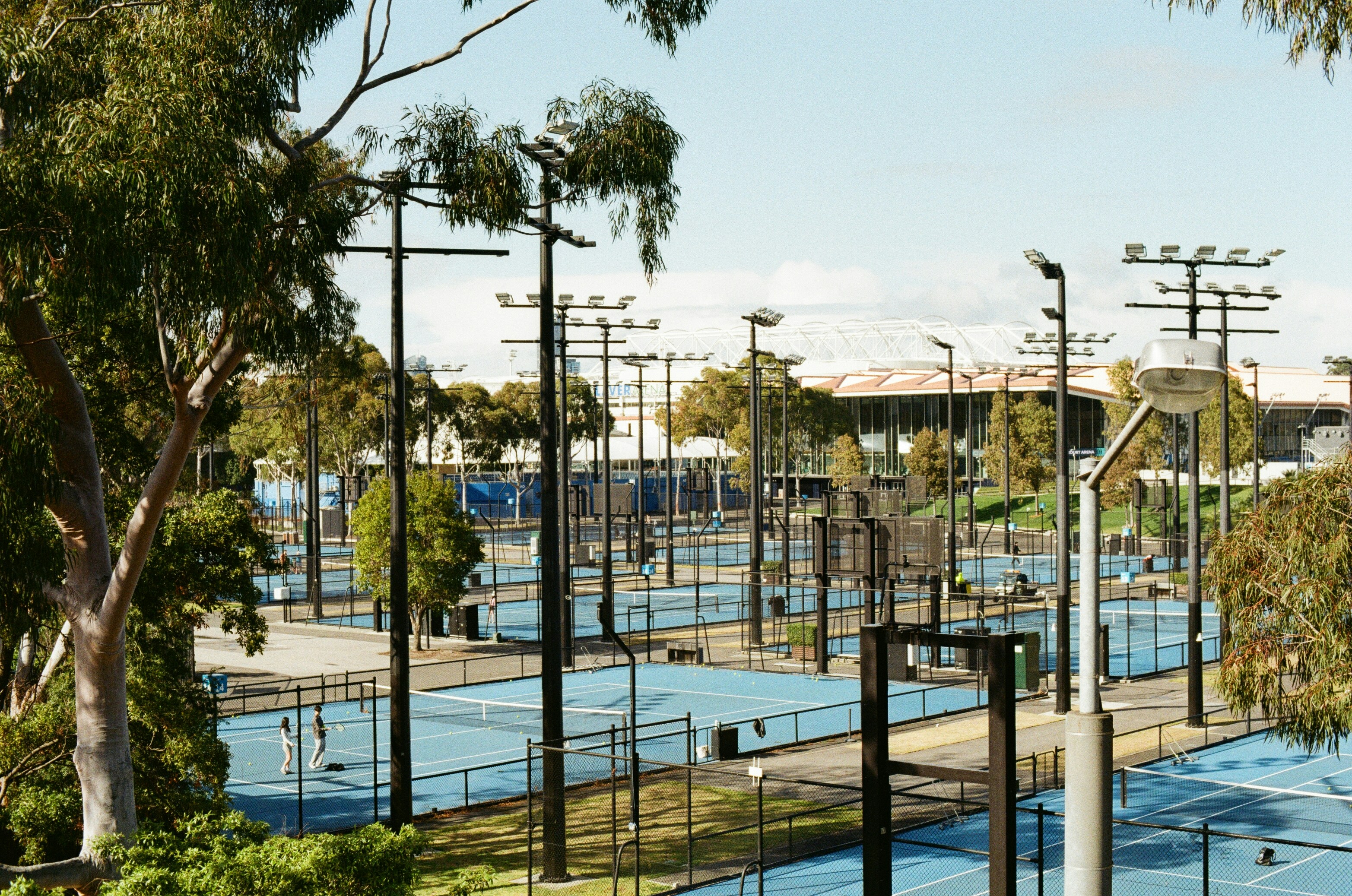 Numerous blue tennis courts with lights and stadium lights
