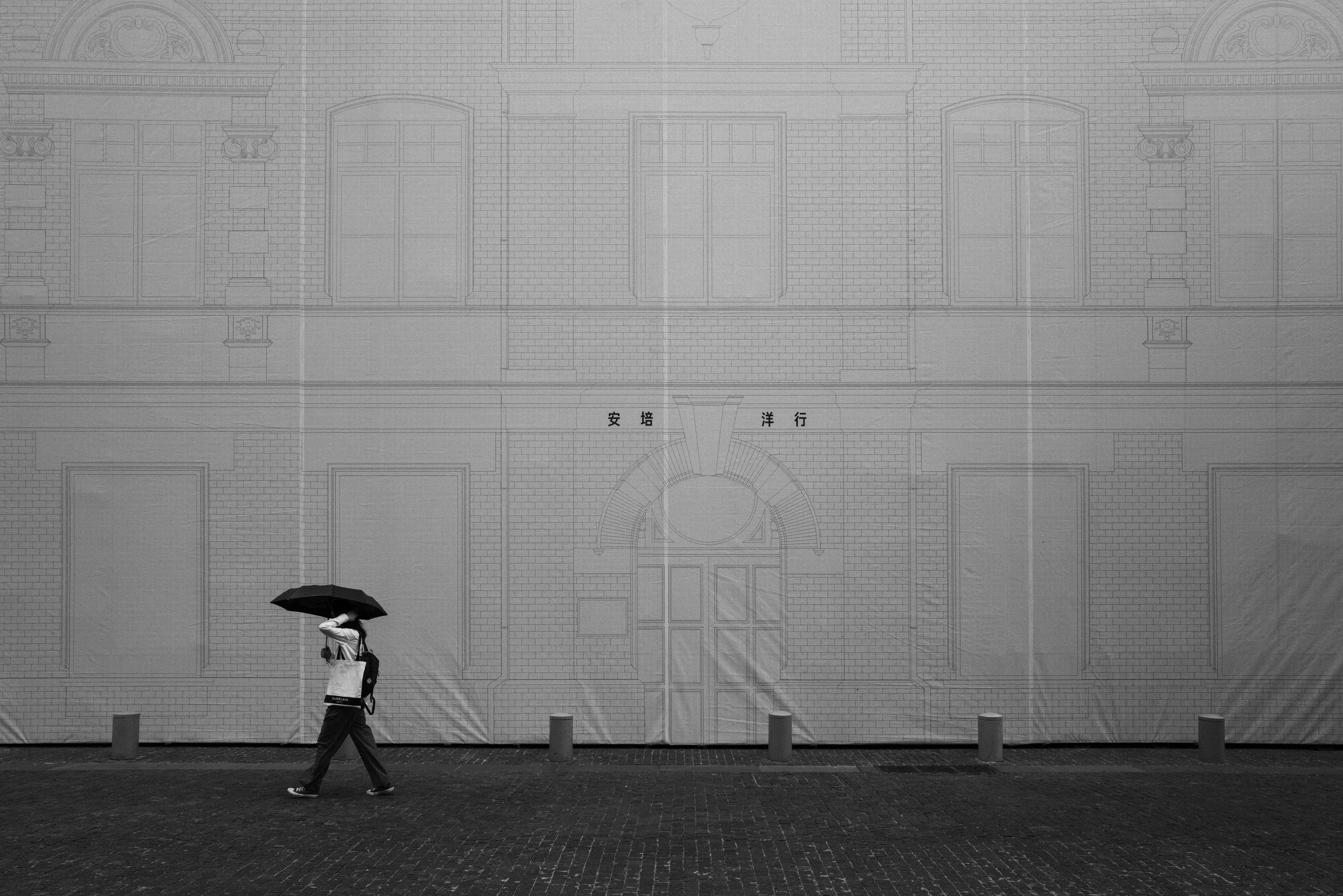 Person with umbrella walks against large building facade.