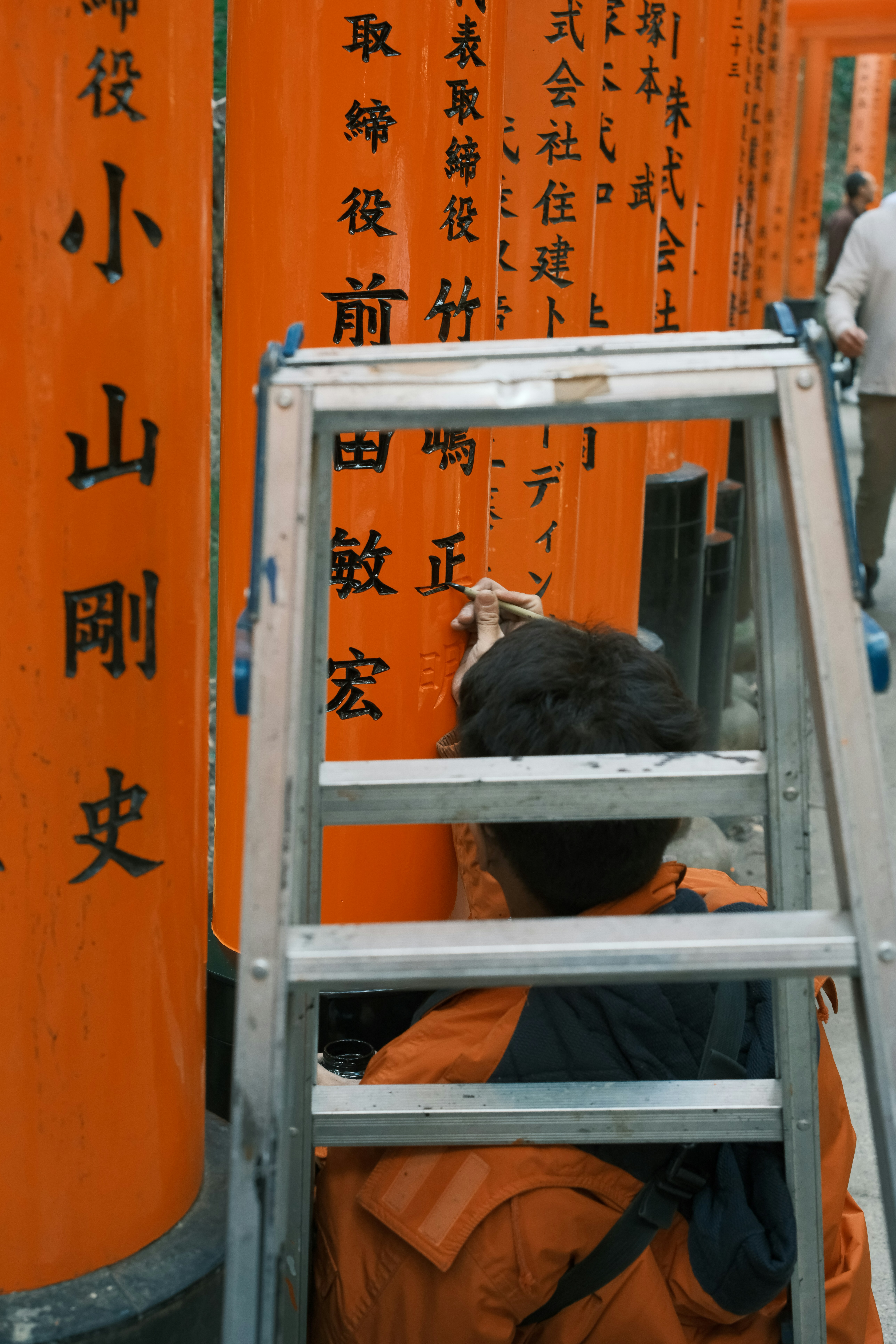 Person on ladder cleaning orange torii gates with writing.