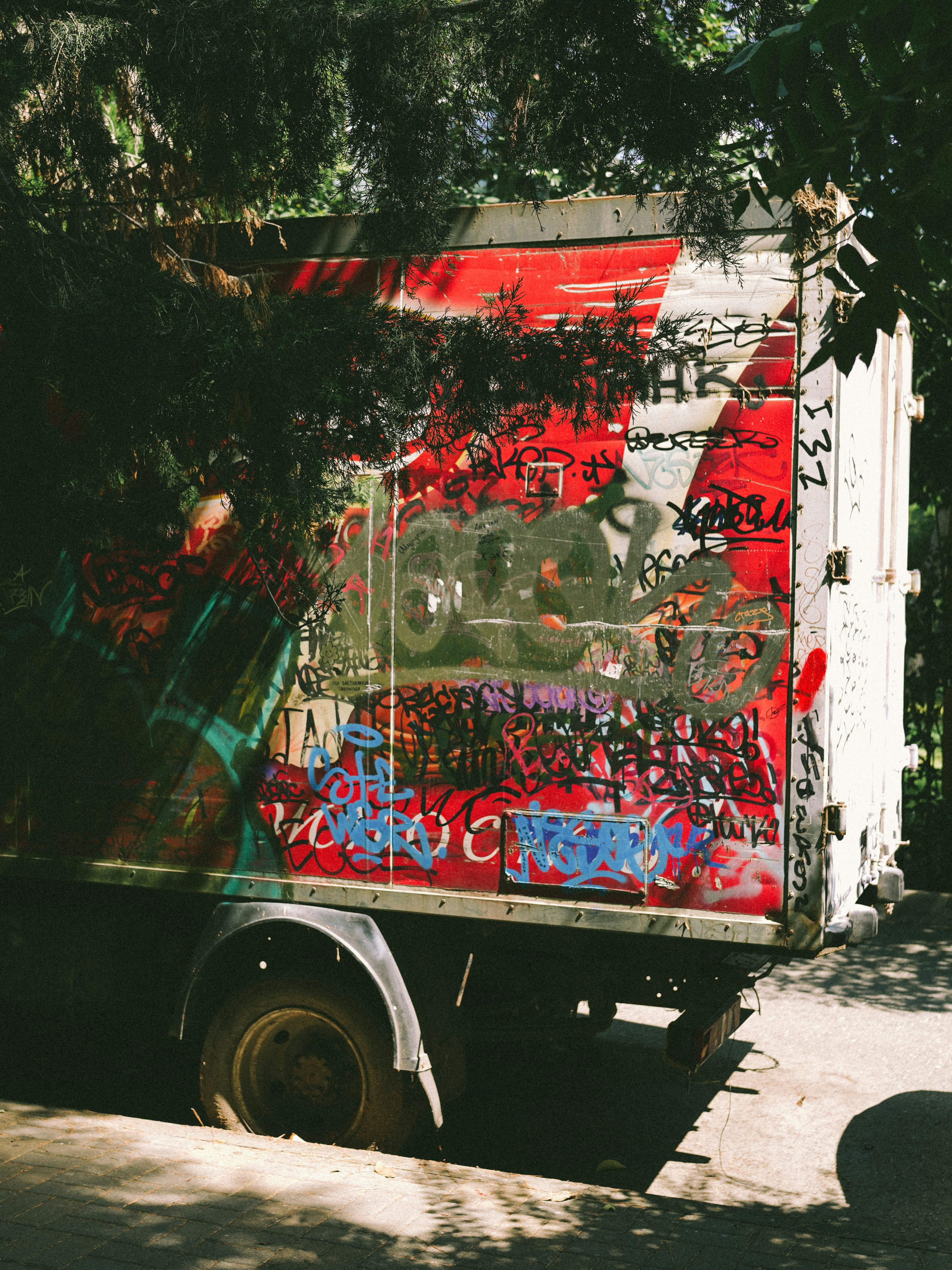 Camion couvert de graffitis garé dans une zone ensoleillée et bordée d’arbres