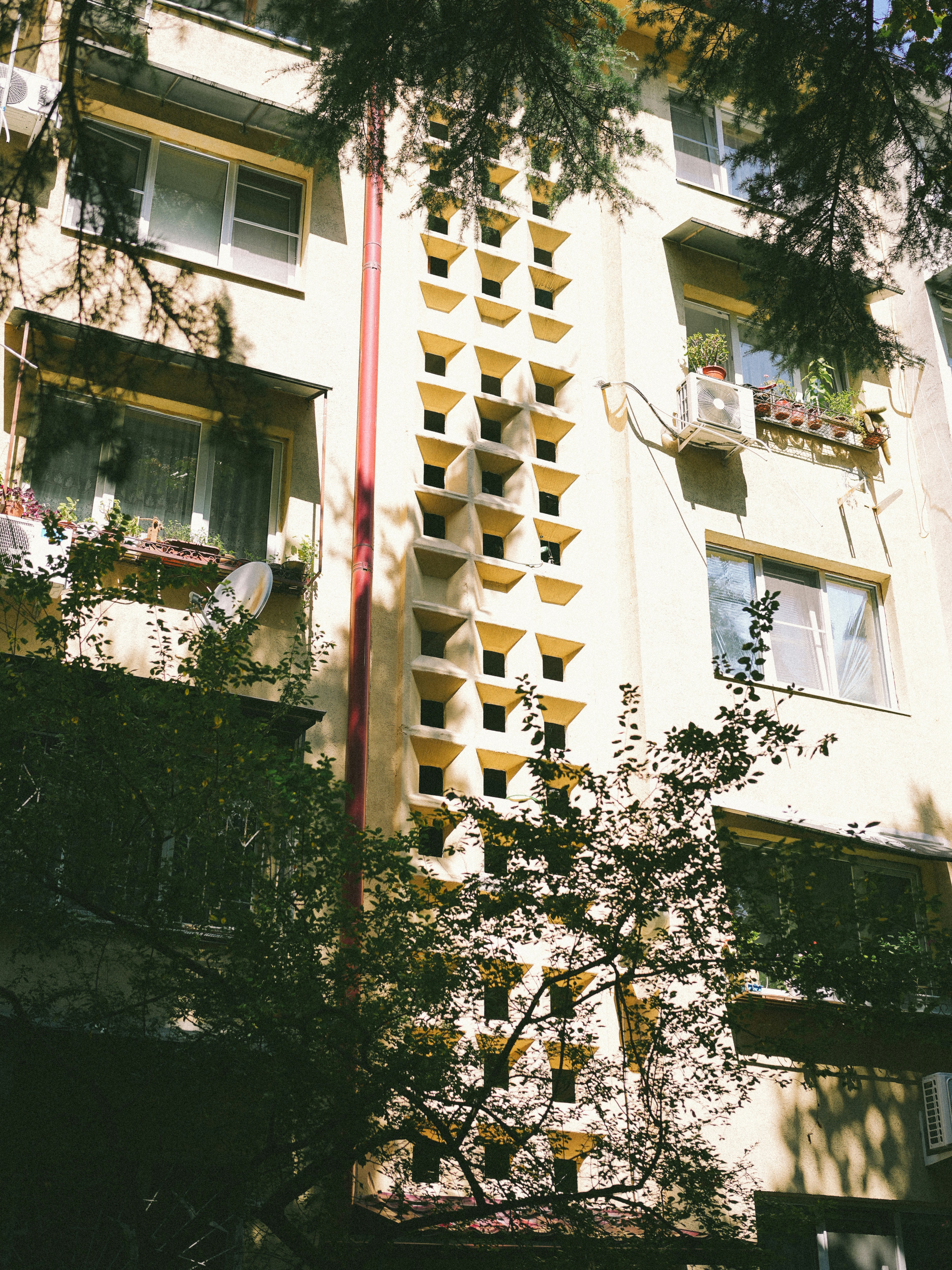 Immeuble d’appartements jaune avec des fenêtres à motifs et des arbres.