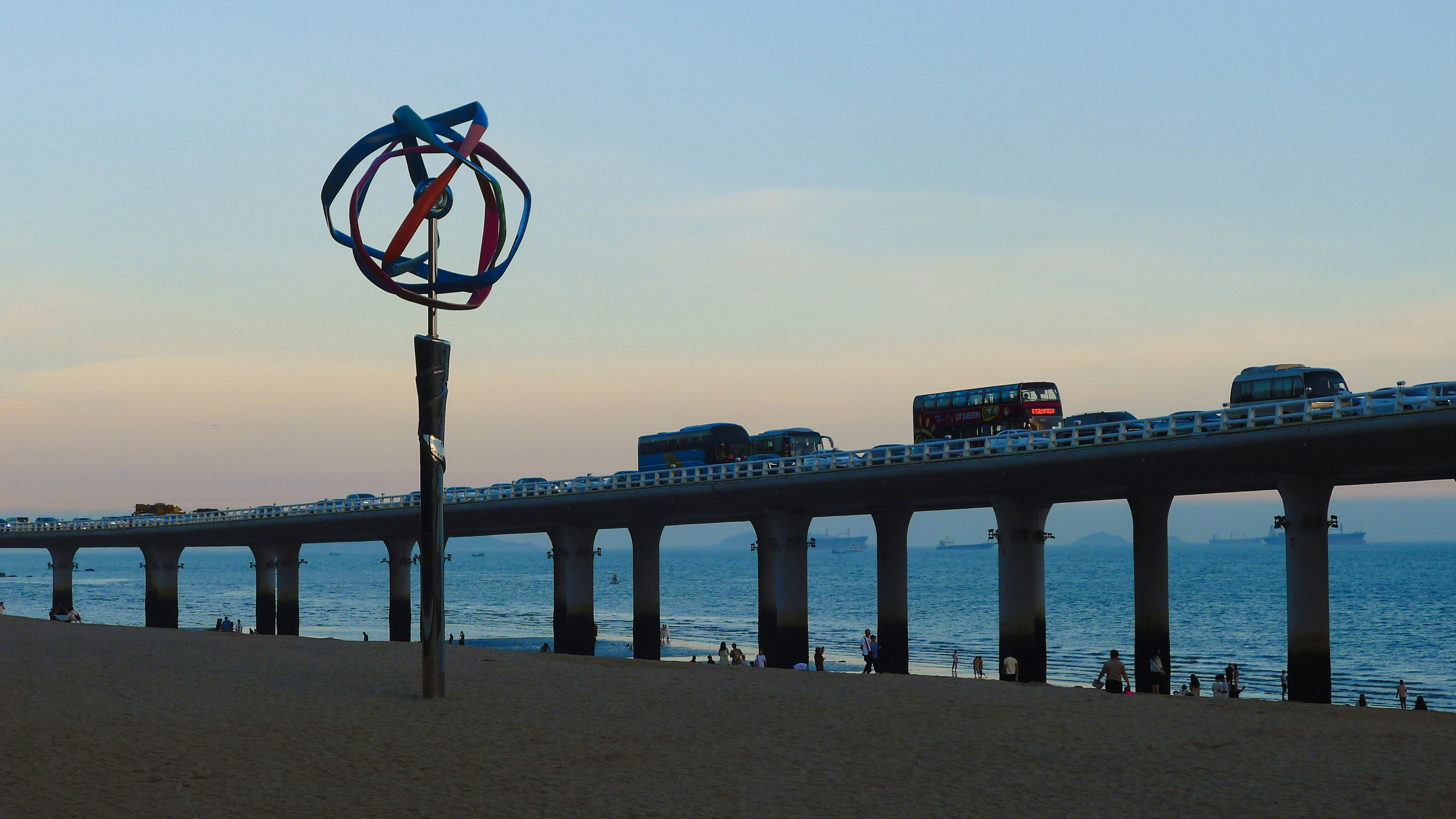 Pier with traffic and a wind sculpture at sunset, 