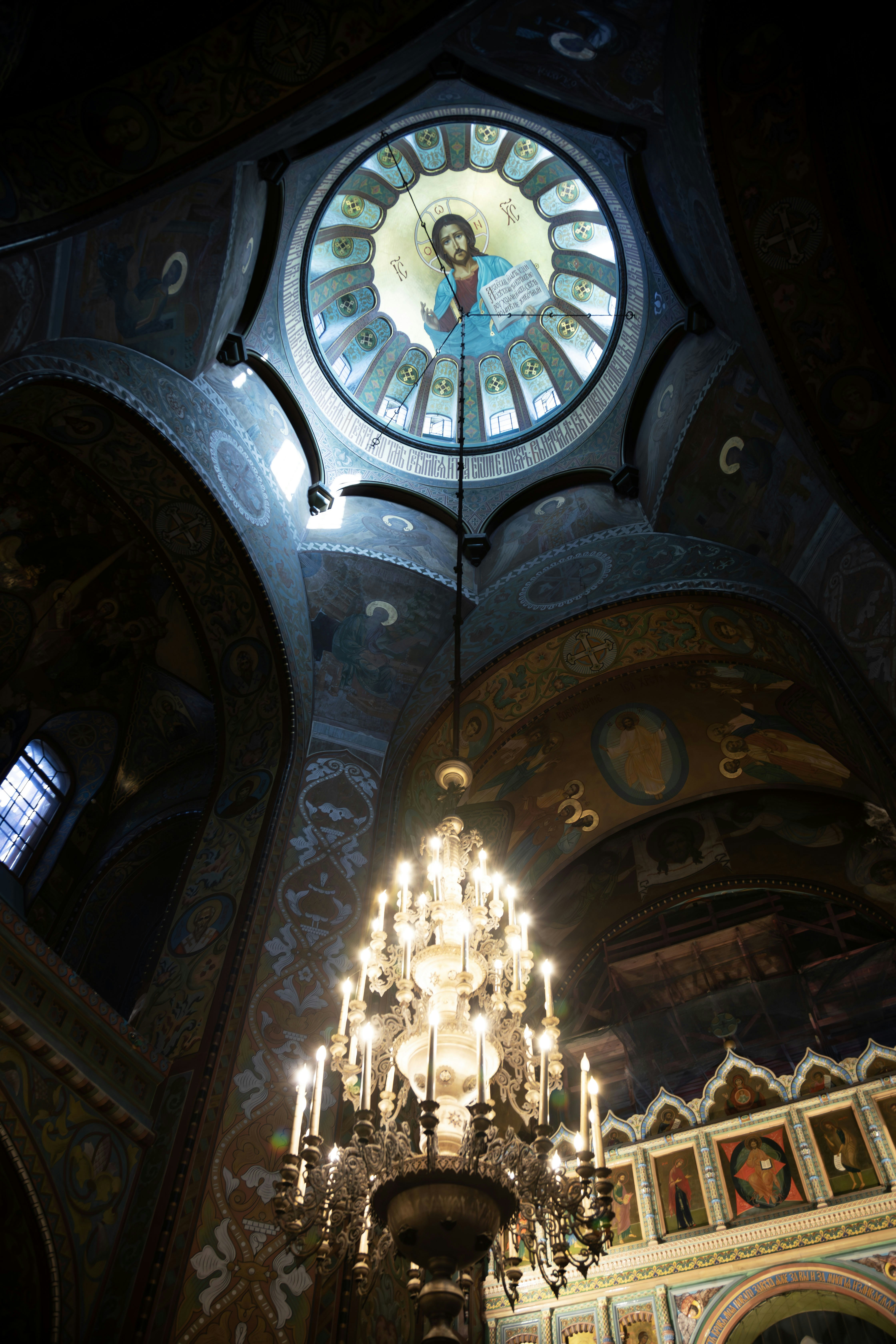Ornate chandelier hangs below a domed ceiling with religious art.