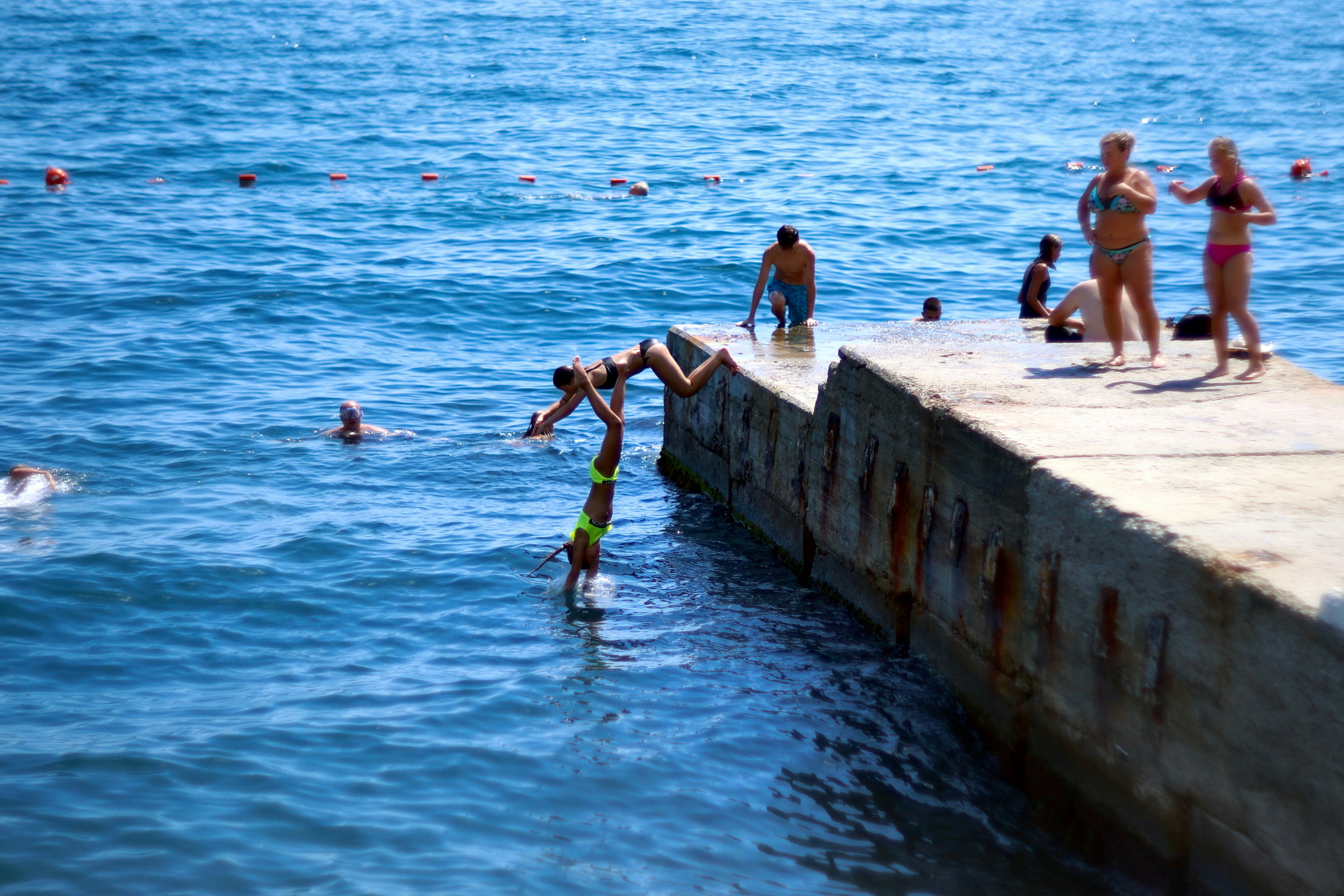 People jumping off pier into blue ocean water