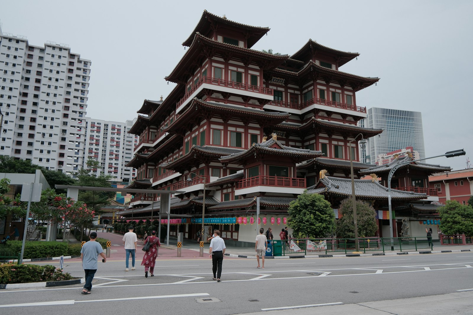 The tiered red-and-dark-roofed facade of the Buddha Tooth Relic Temple in Chinatown, with pedestrians crossing the street in front