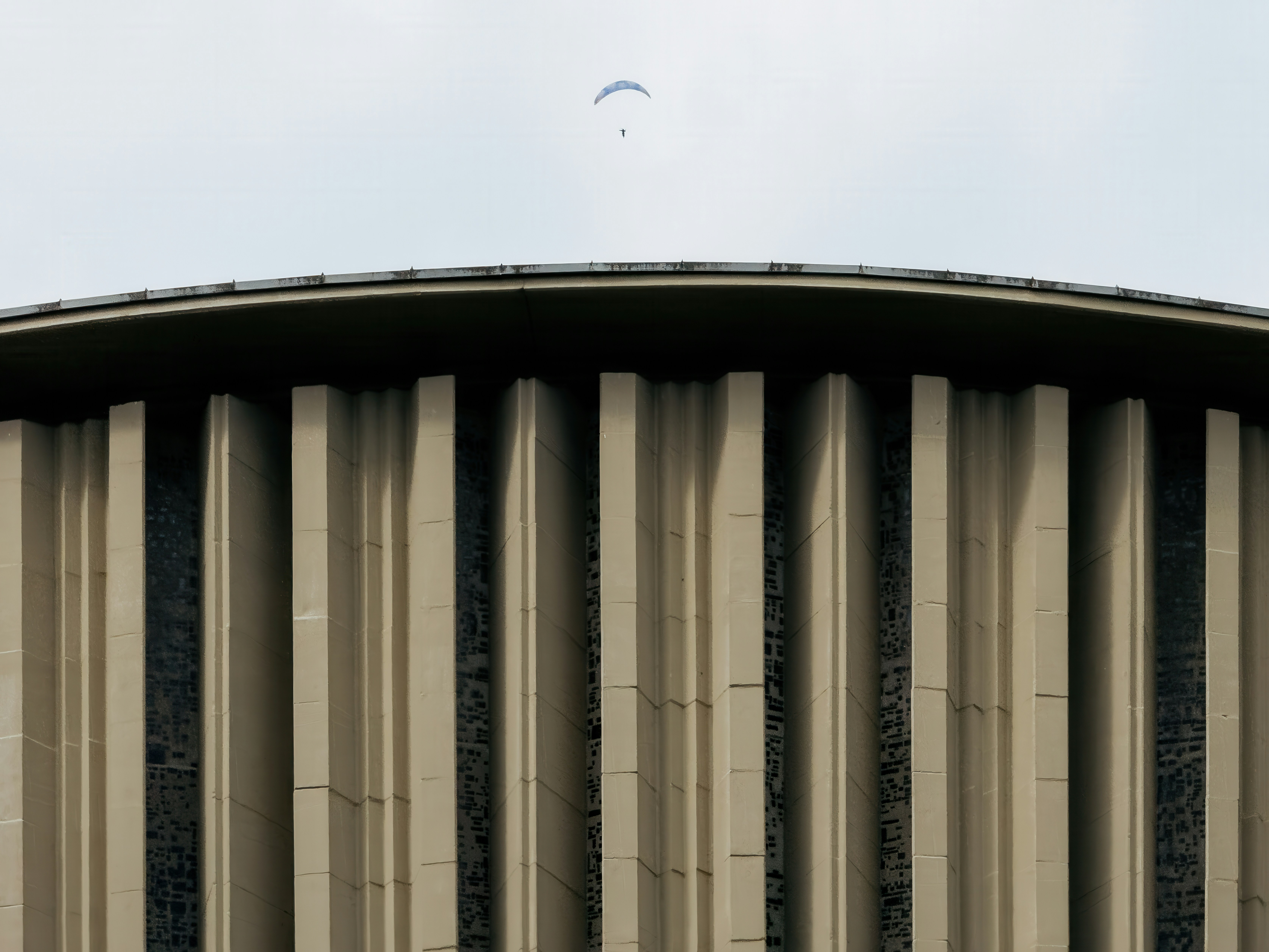 Parapente voa acima de uma fachada curva de edifício.