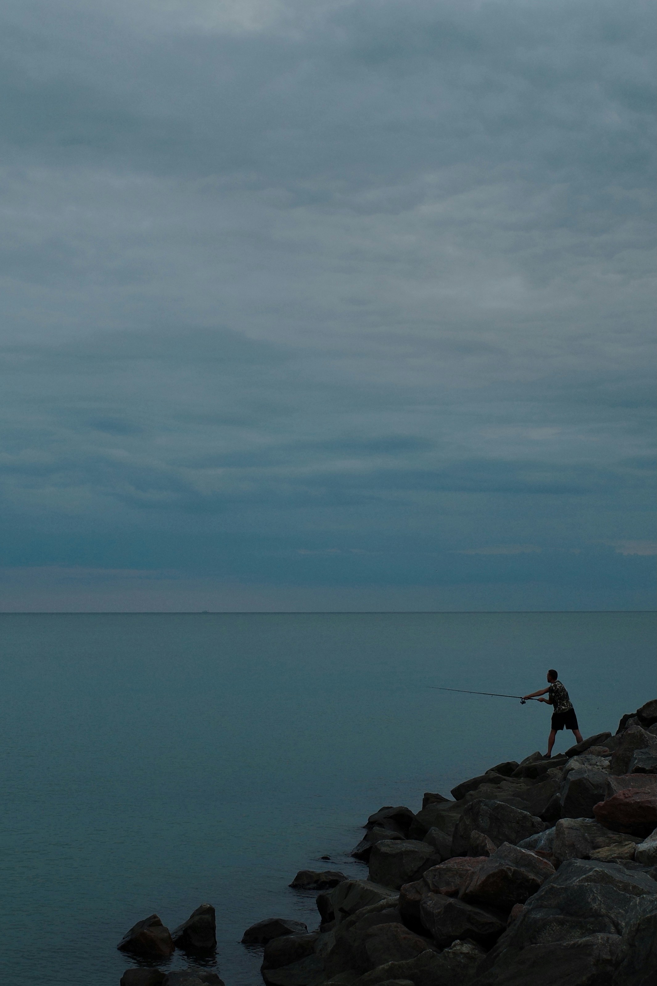 Man fishing from rocky shore under cloudy sky
