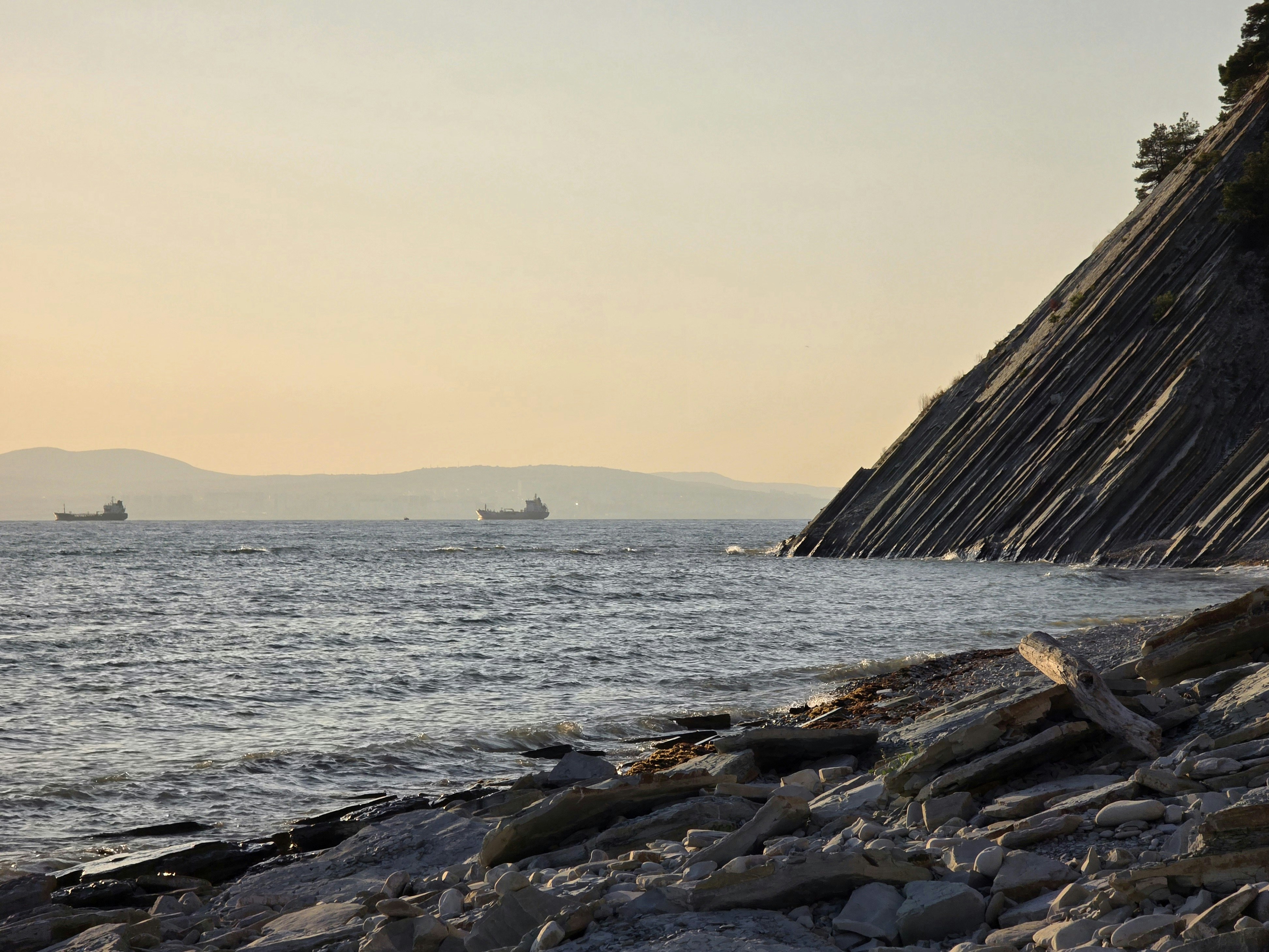 Ships on the ocean near a rocky coastline at sunset