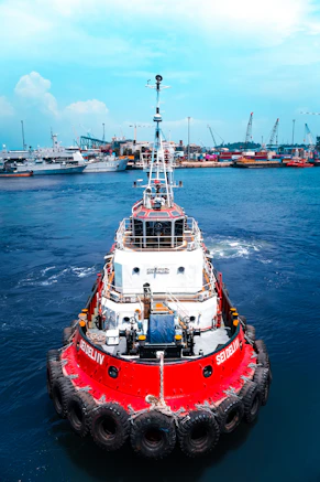 A red and white tugboat moves through blue water.