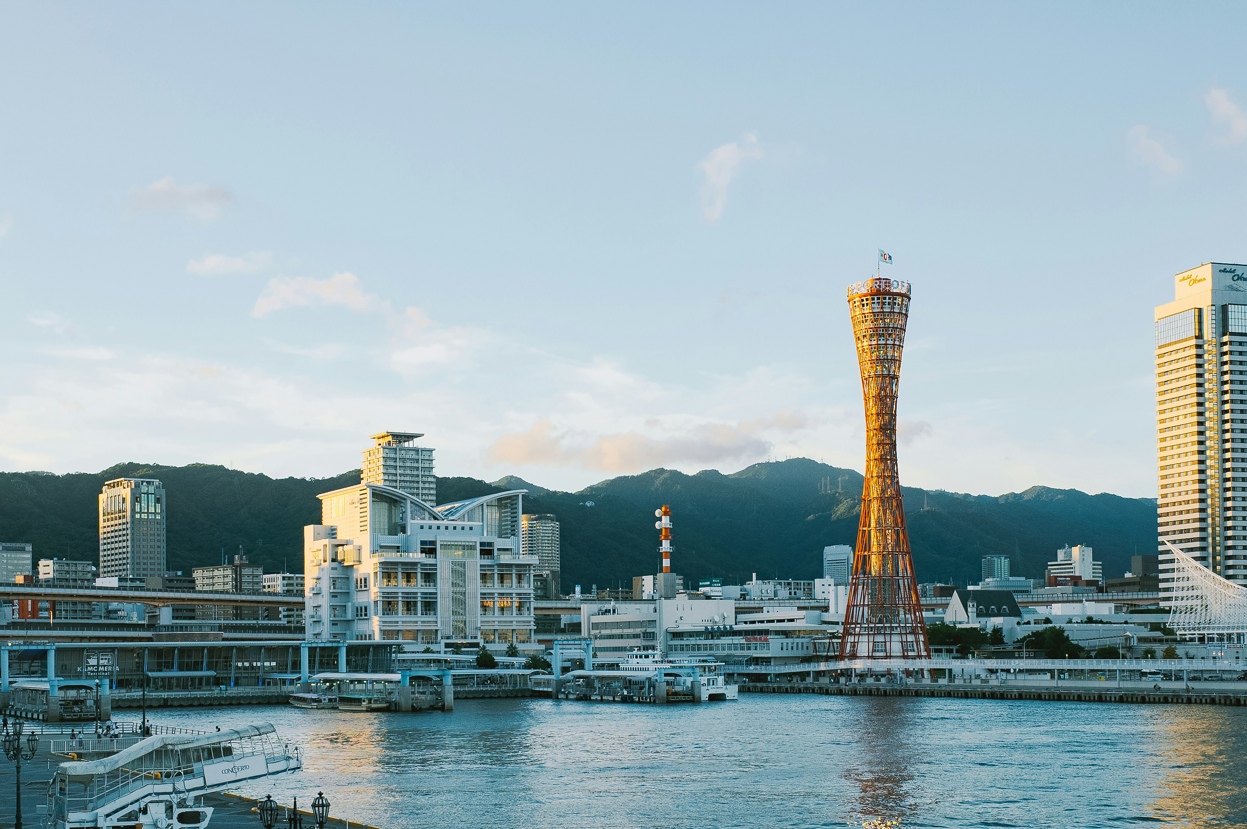 Modern cityscape with a tall tower and mountains.