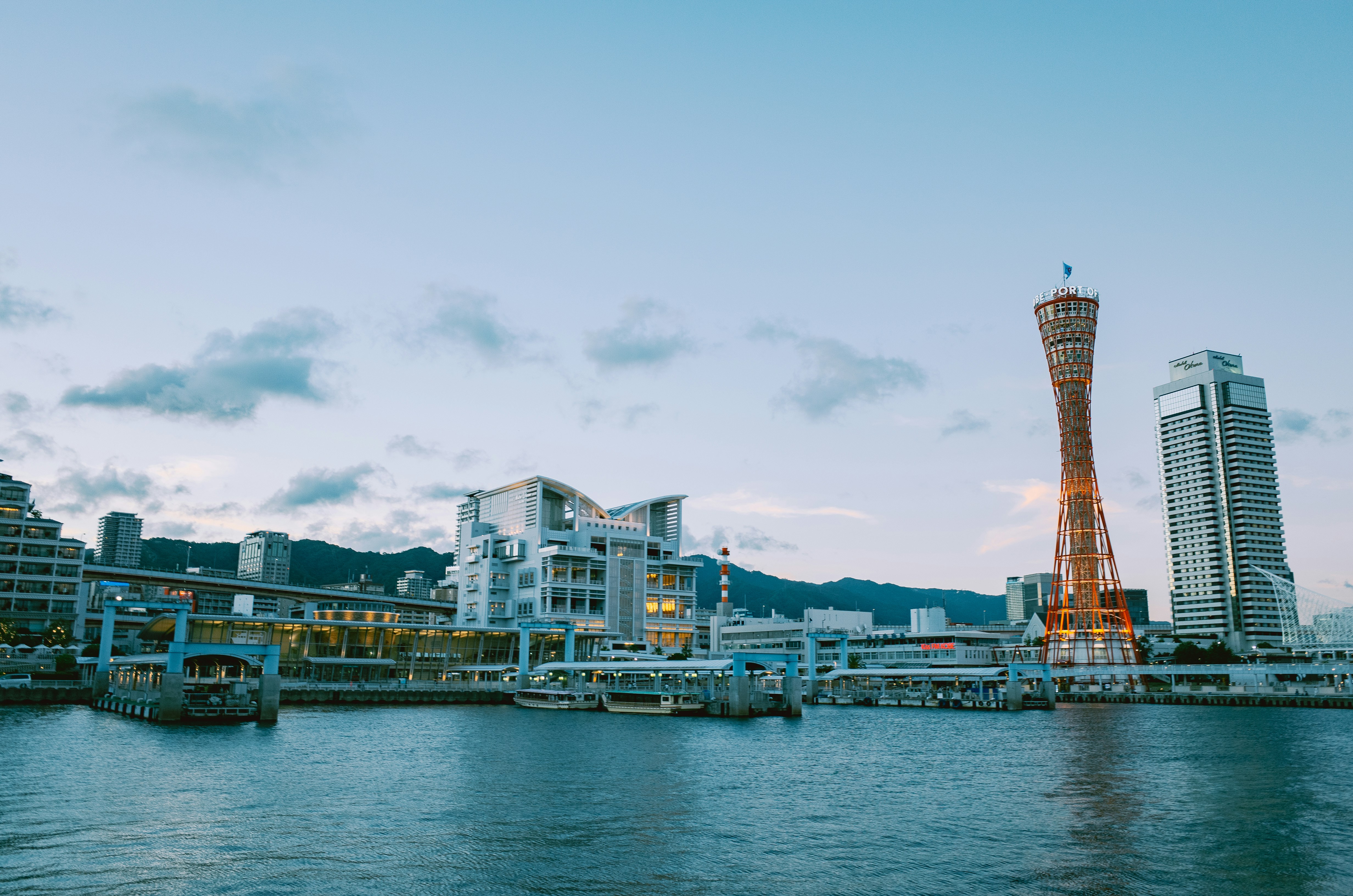 Harbor with modern buildings and a tall tower at dusk.