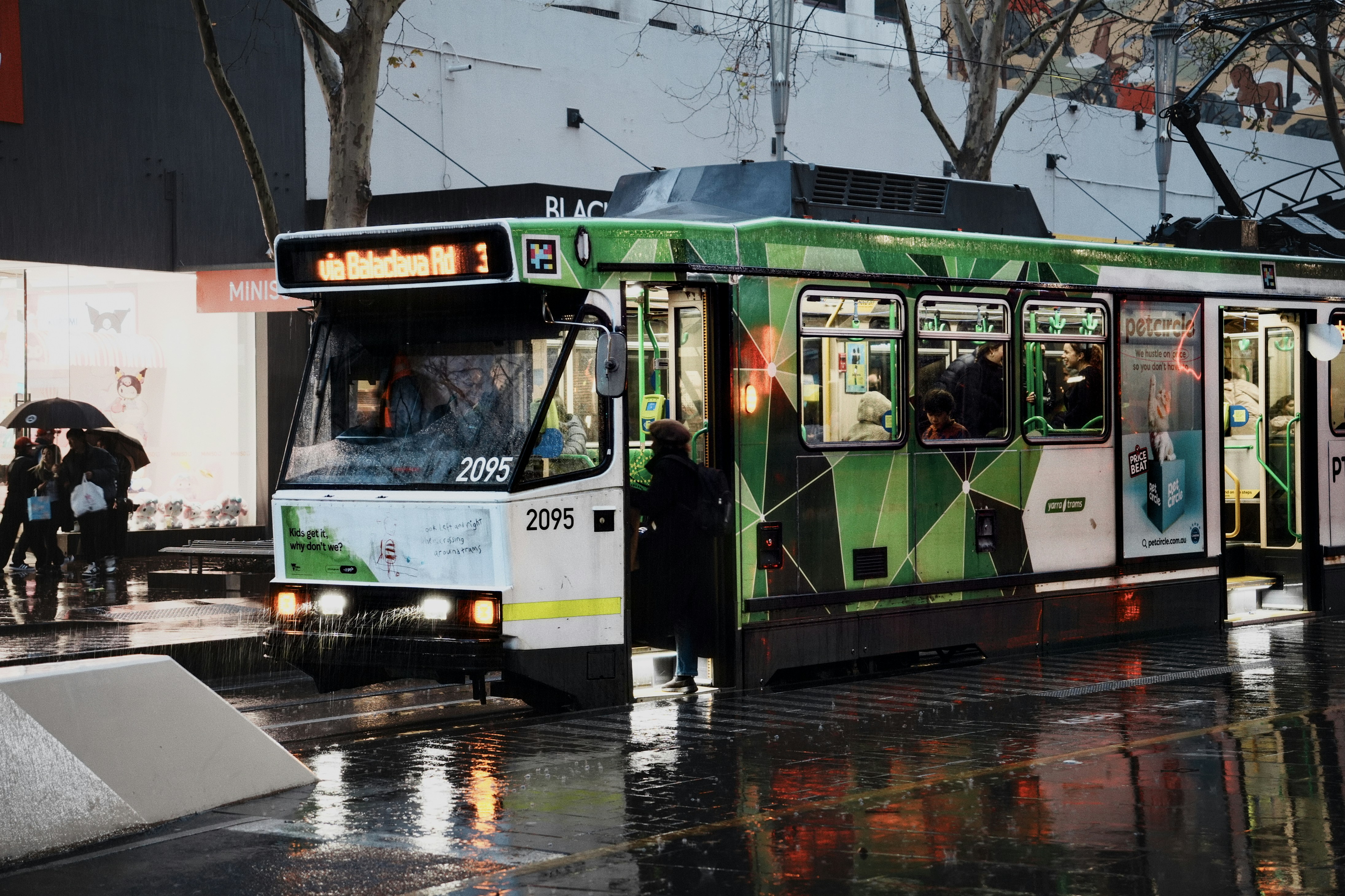 Green tram with passengers on a wet city street.