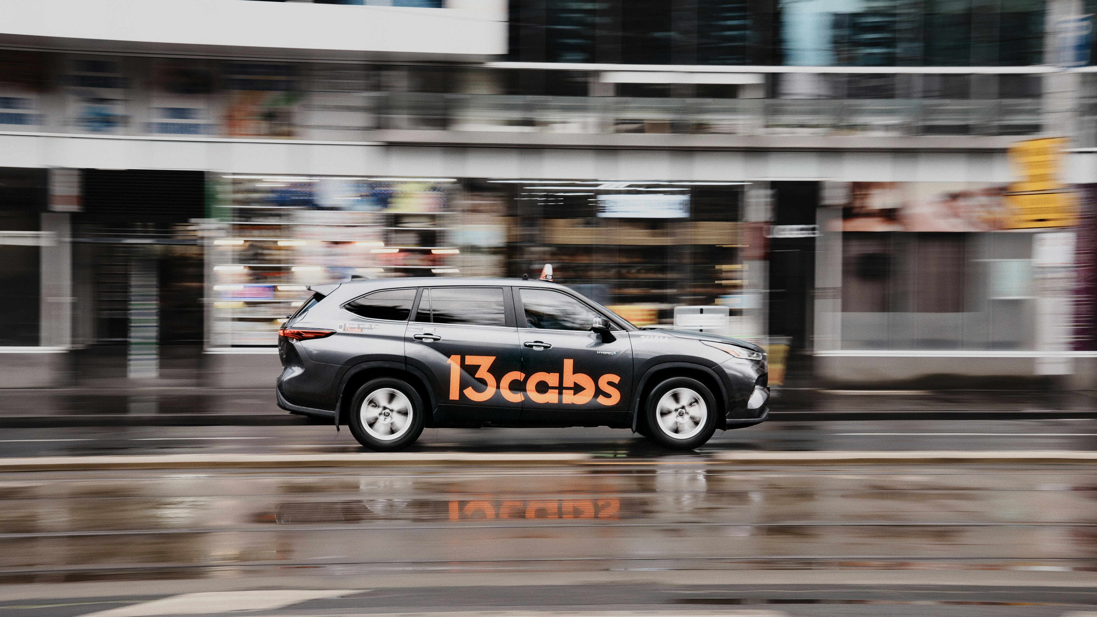 Ein dunkler SUV mit dem Branding "13cabs" fährt auf nasser Straße.
