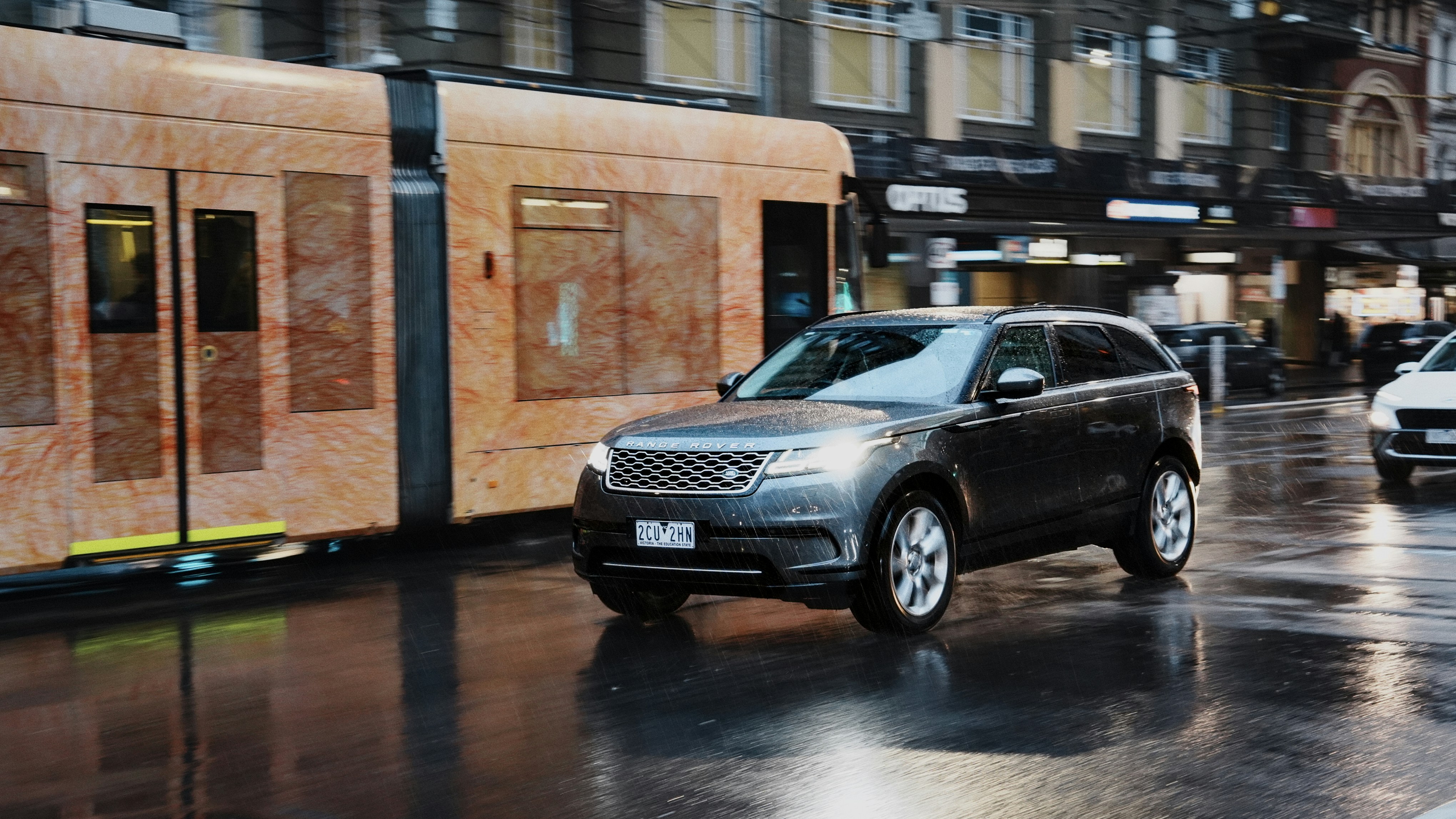 Ein Auto fährt auf nasser Straße an einer Straßenbahn vorbei.