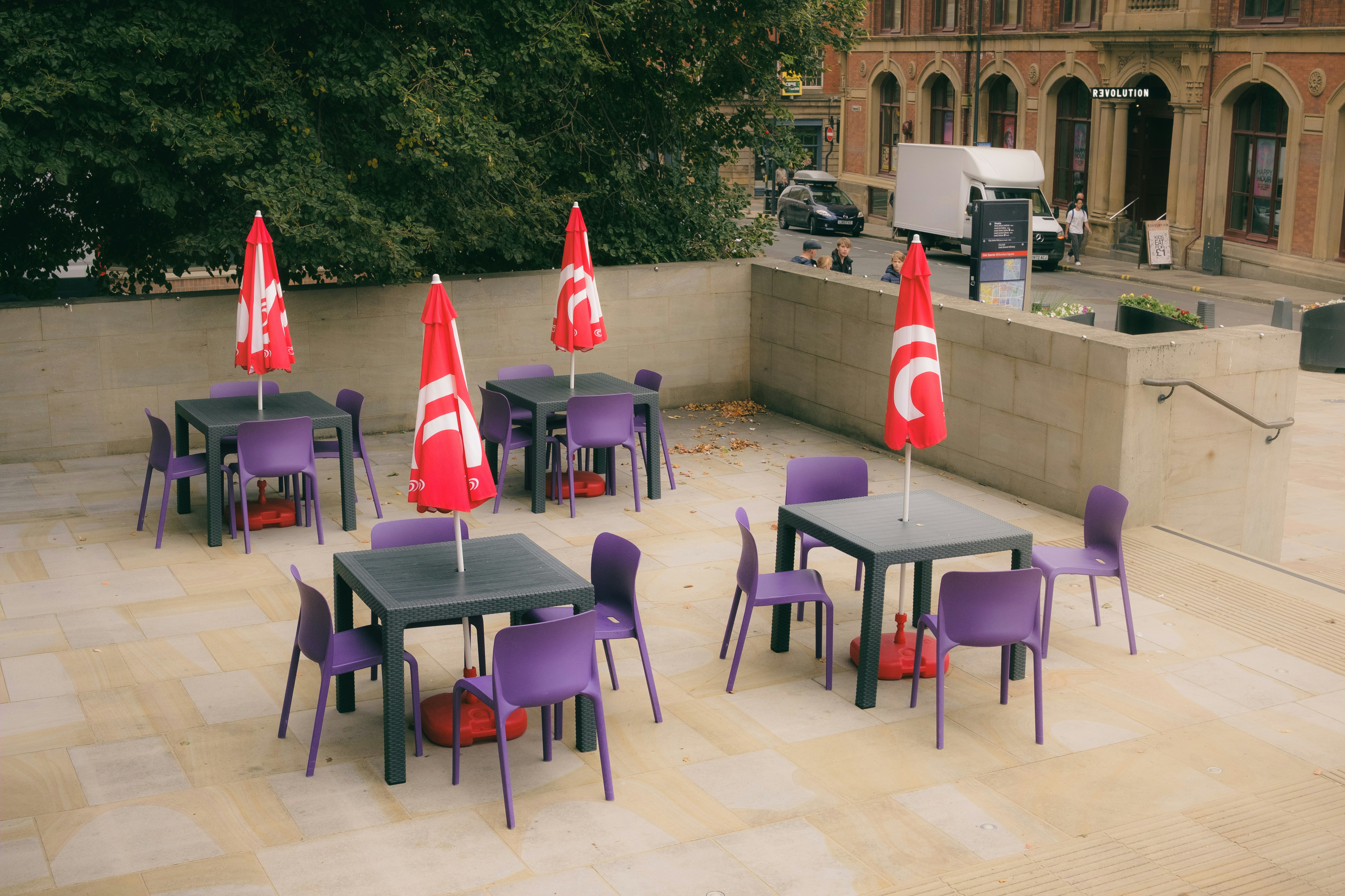 Café-Tische im Freien mit lila Stühlen und roten Sonnenschirmen