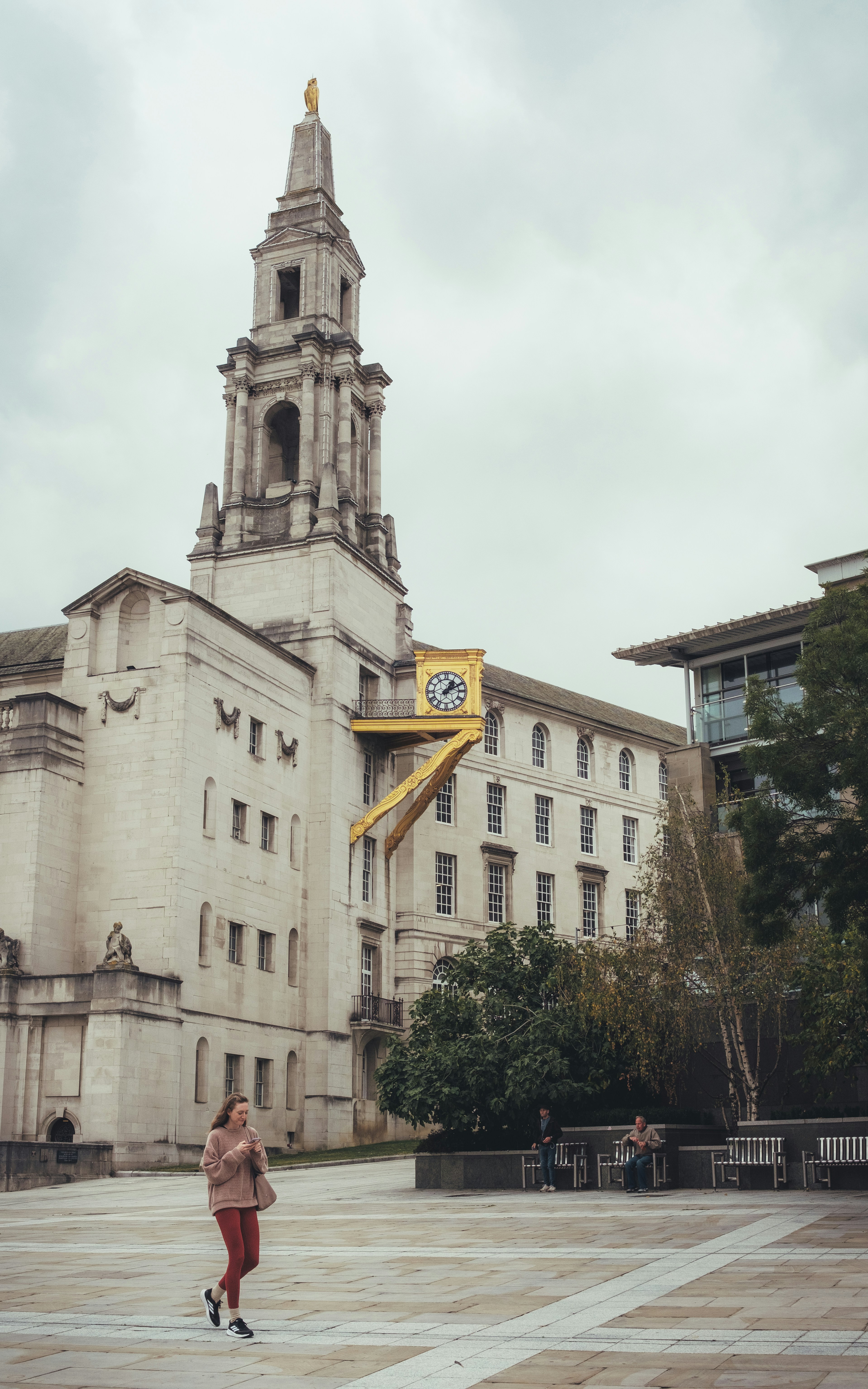 Frau geht am Gebäude mit markanter goldener Uhr vorbei.