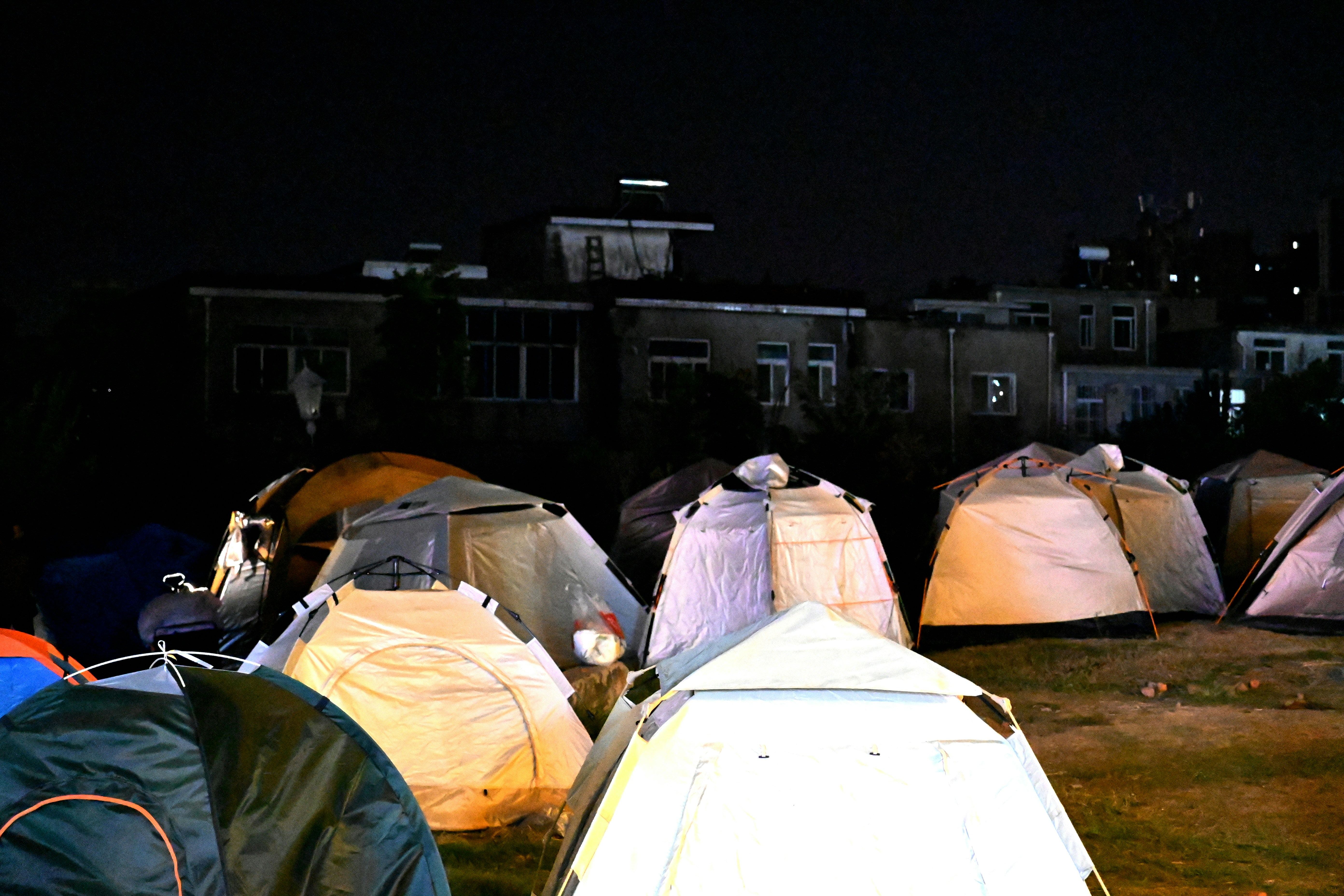 Tents set up at night with buildings in background