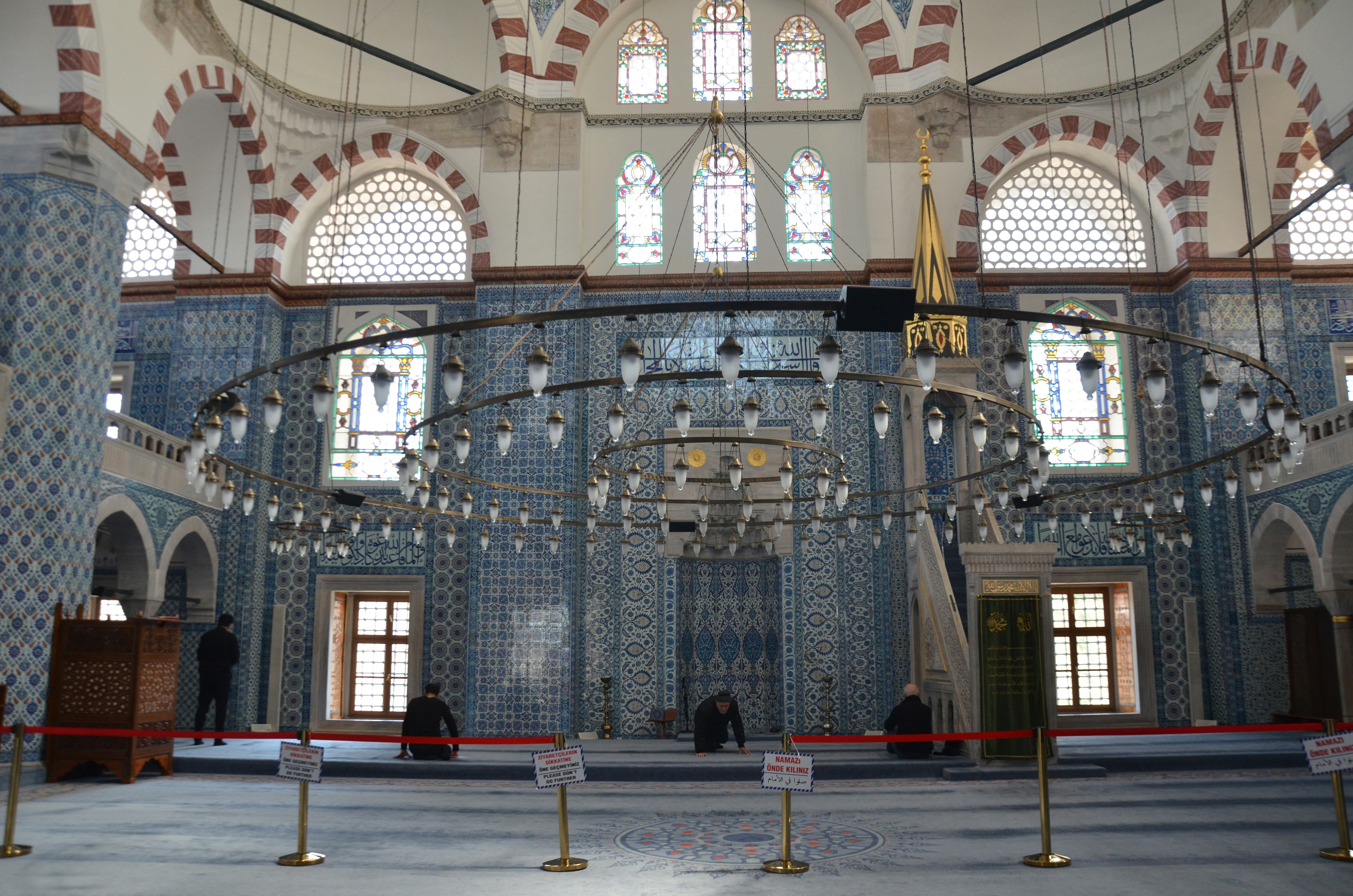 Interior of a mosque with ornate tilework and chandelier.