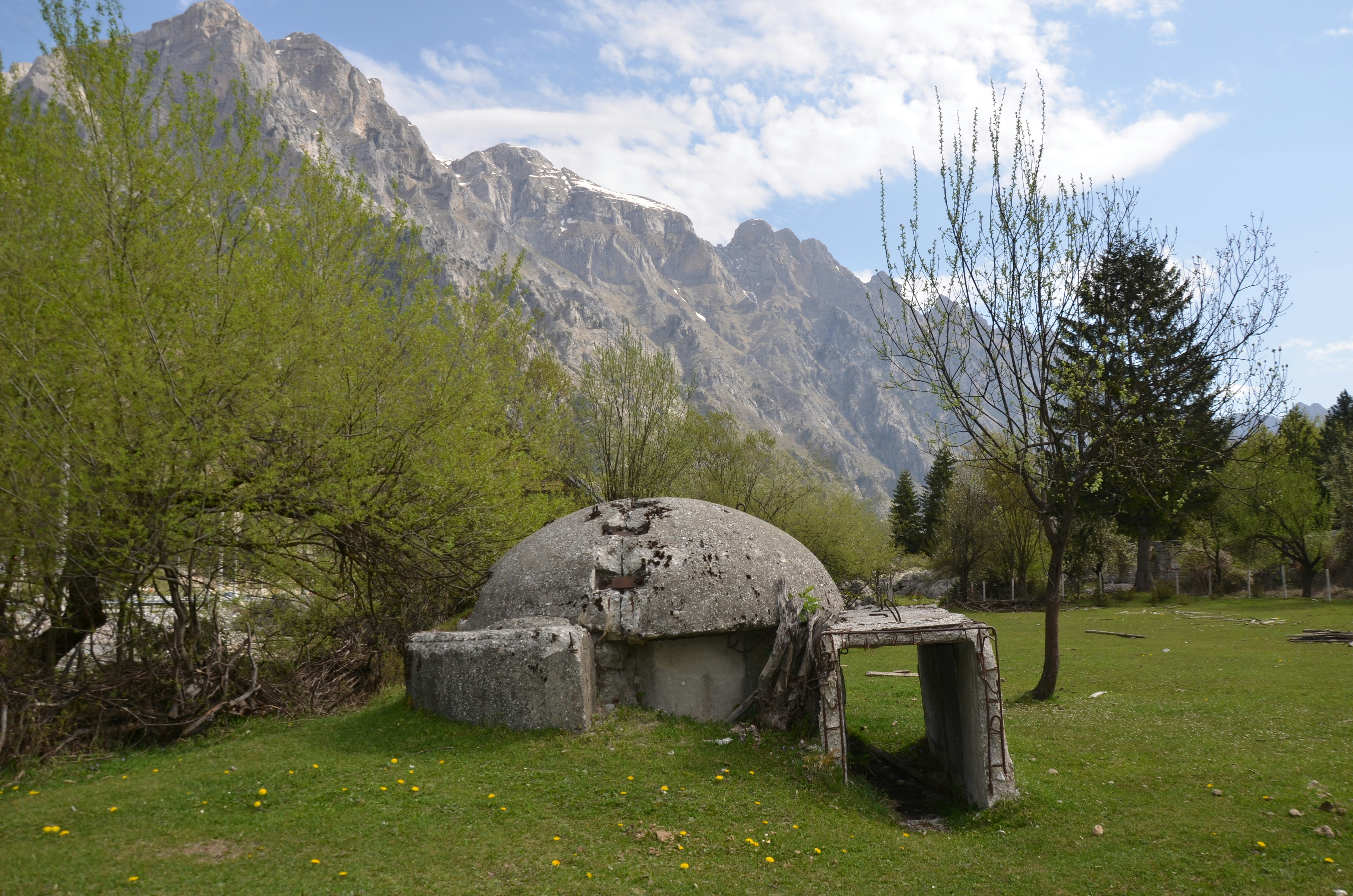 Abandoned bunker in a grassy field with mountains behind.