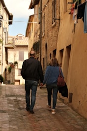 Couple holding hands walking down cobblestone street.