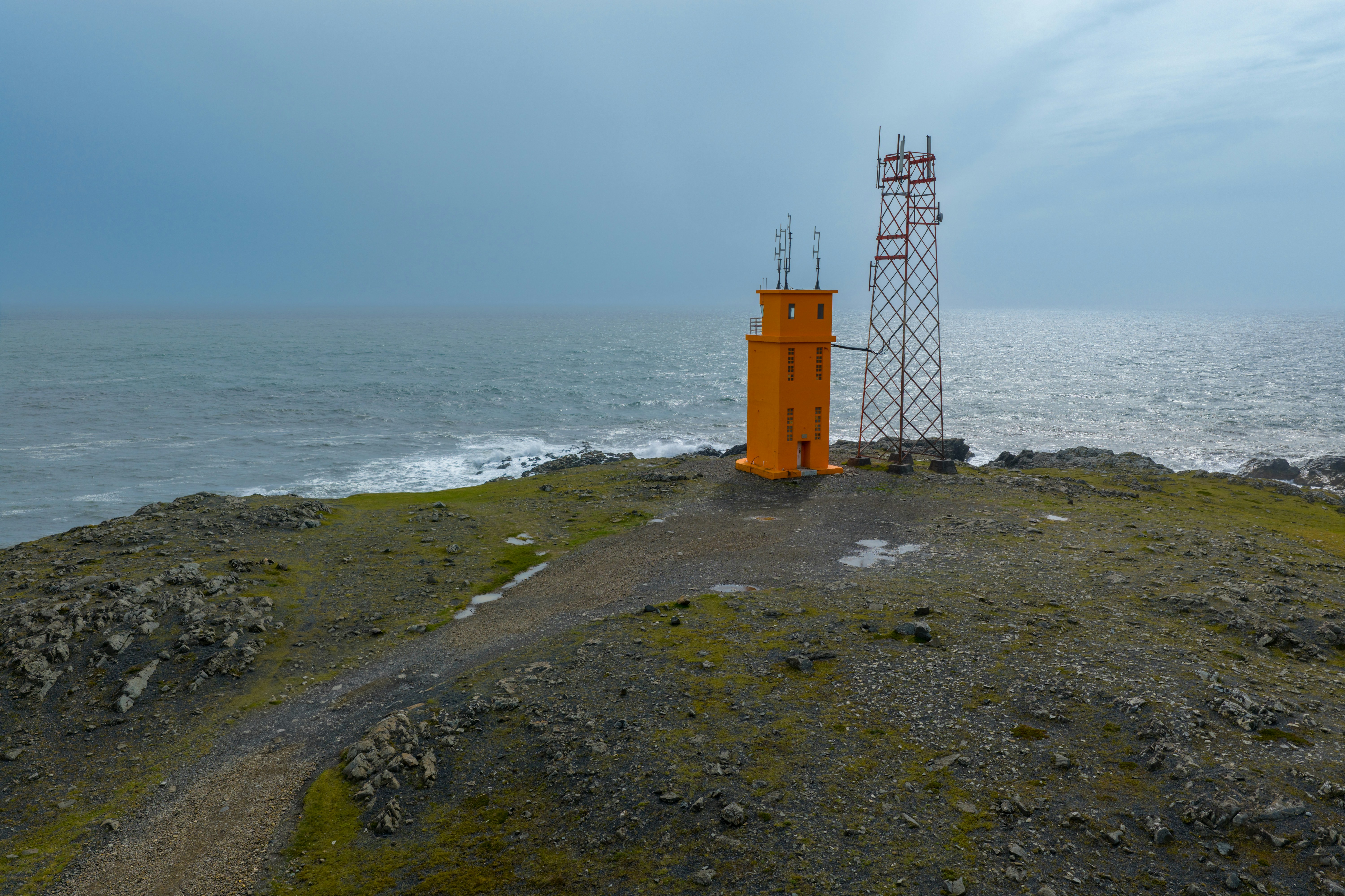 Orange lighthouse and cell tower on rocky coast