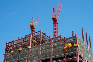 Two red cranes tower over a building construction site.