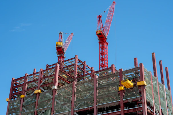 Two red cranes tower over a building construction site.