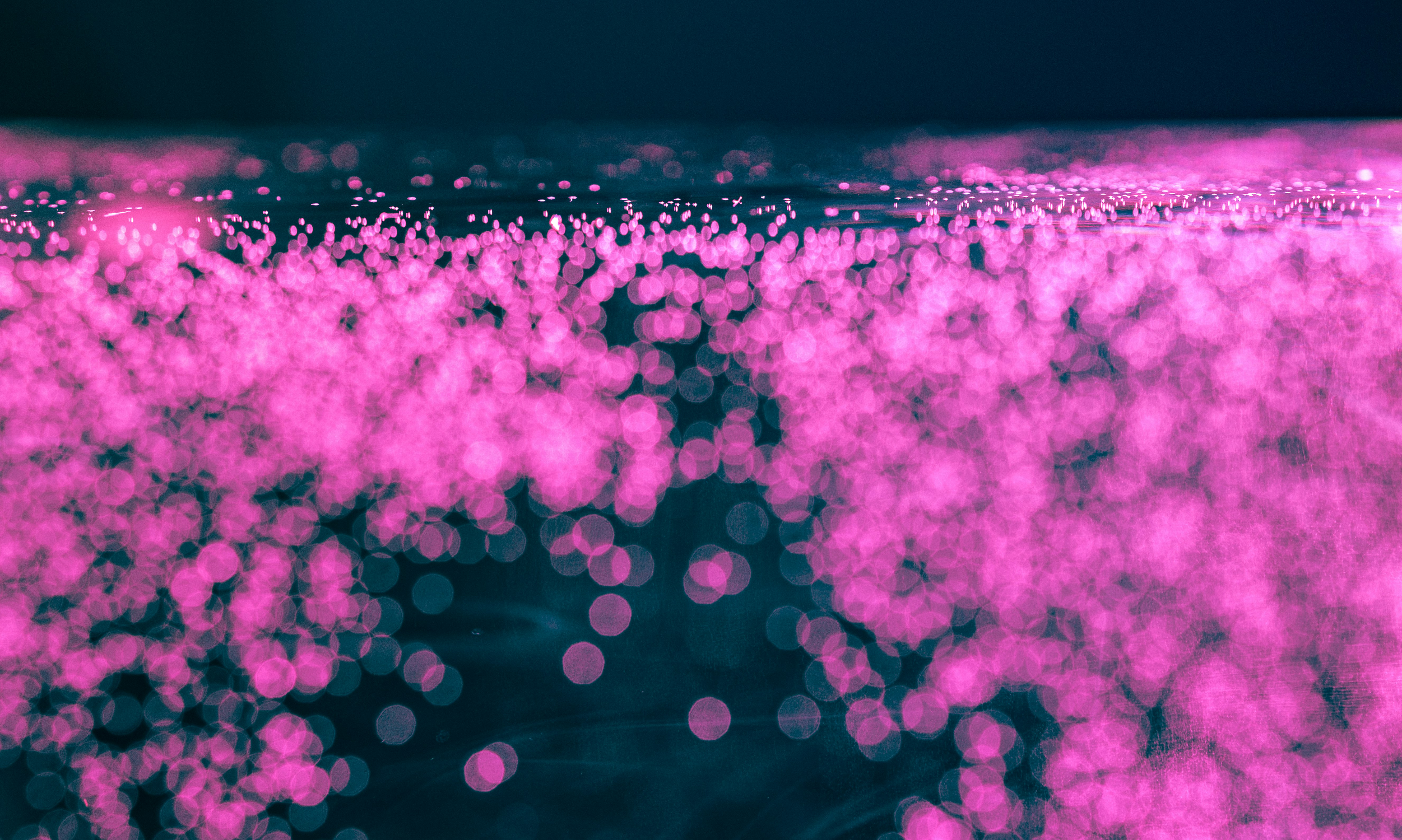 Abstract pink particles floating in dark blue liquid.