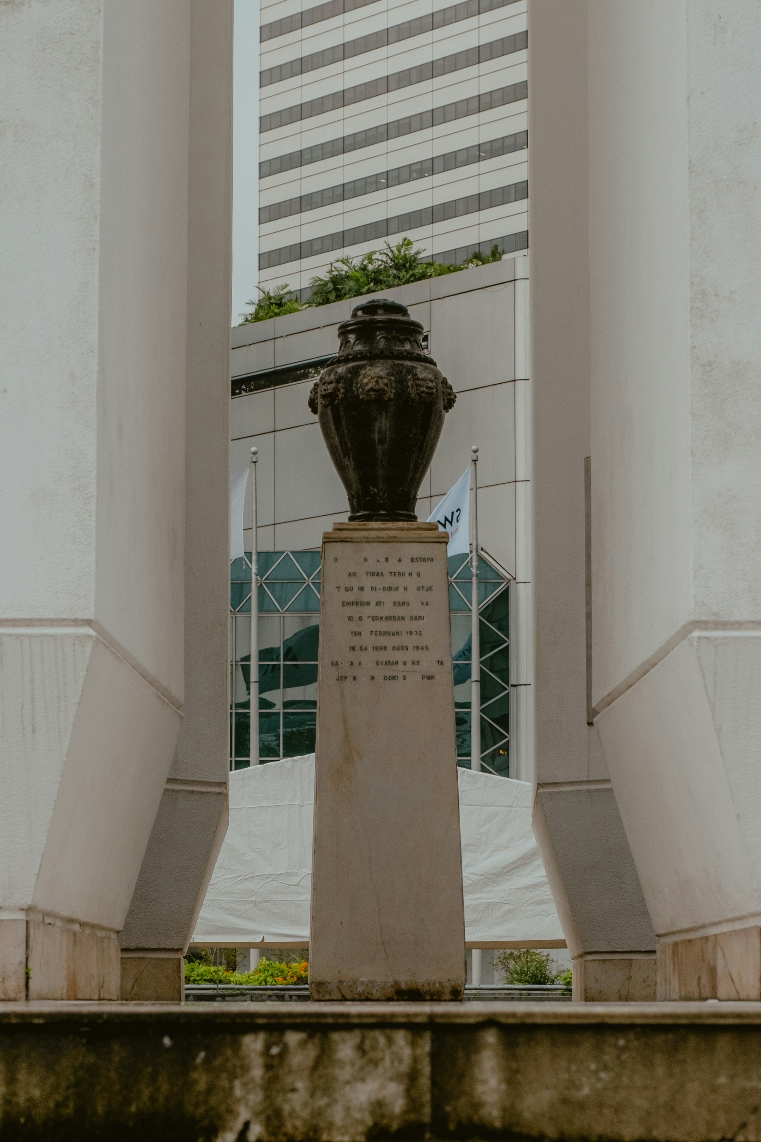 A dark urn sits on a stone pedestal between pillars.