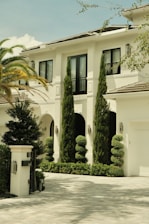 Elegant white mansion with manicured topiaries and palm trees