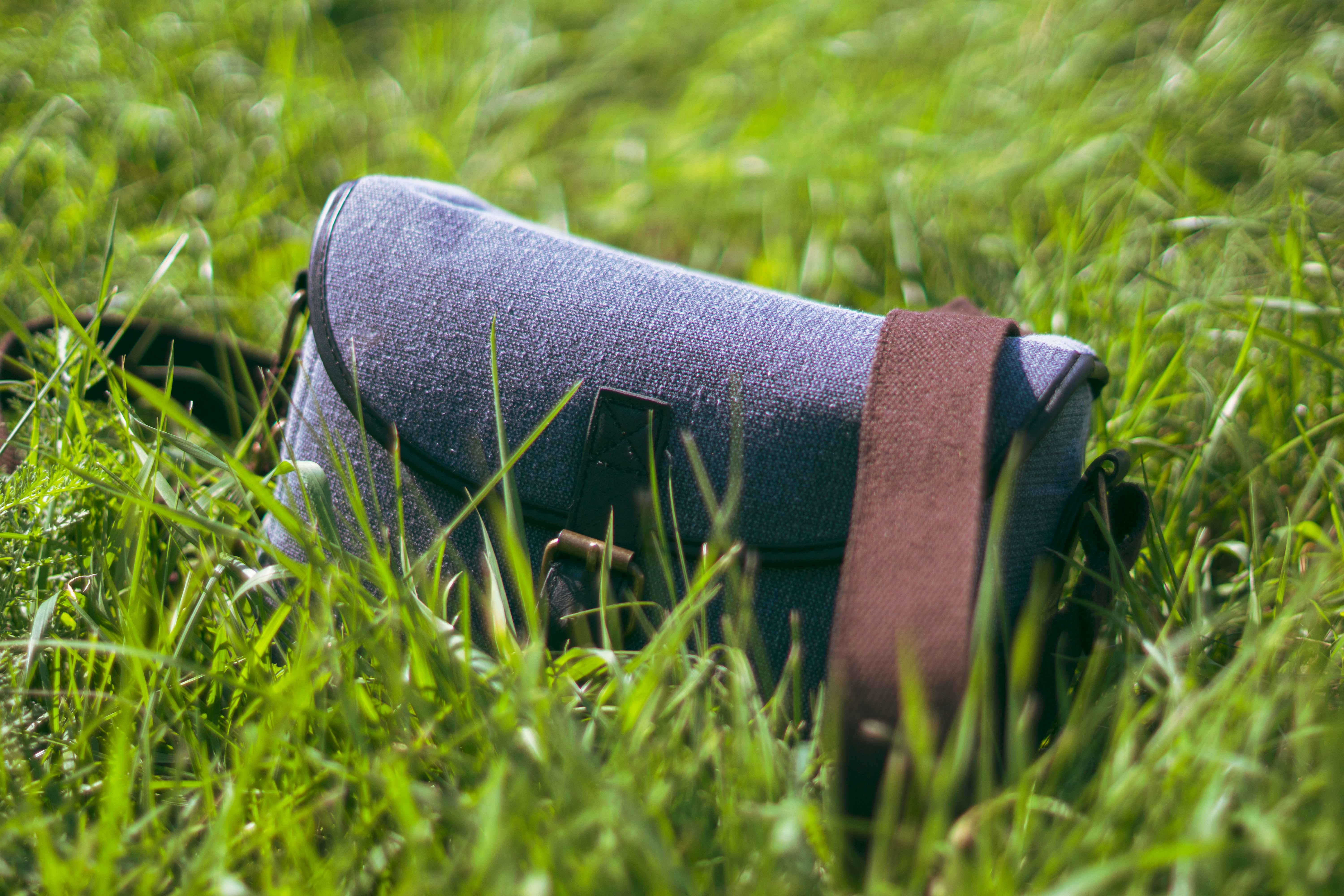 A messenger bag rests in green grass.