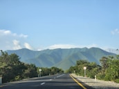 Open road leading towards distant mountains under blue sky.