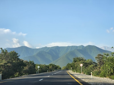 Open road leading towards distant mountains under blue sky.