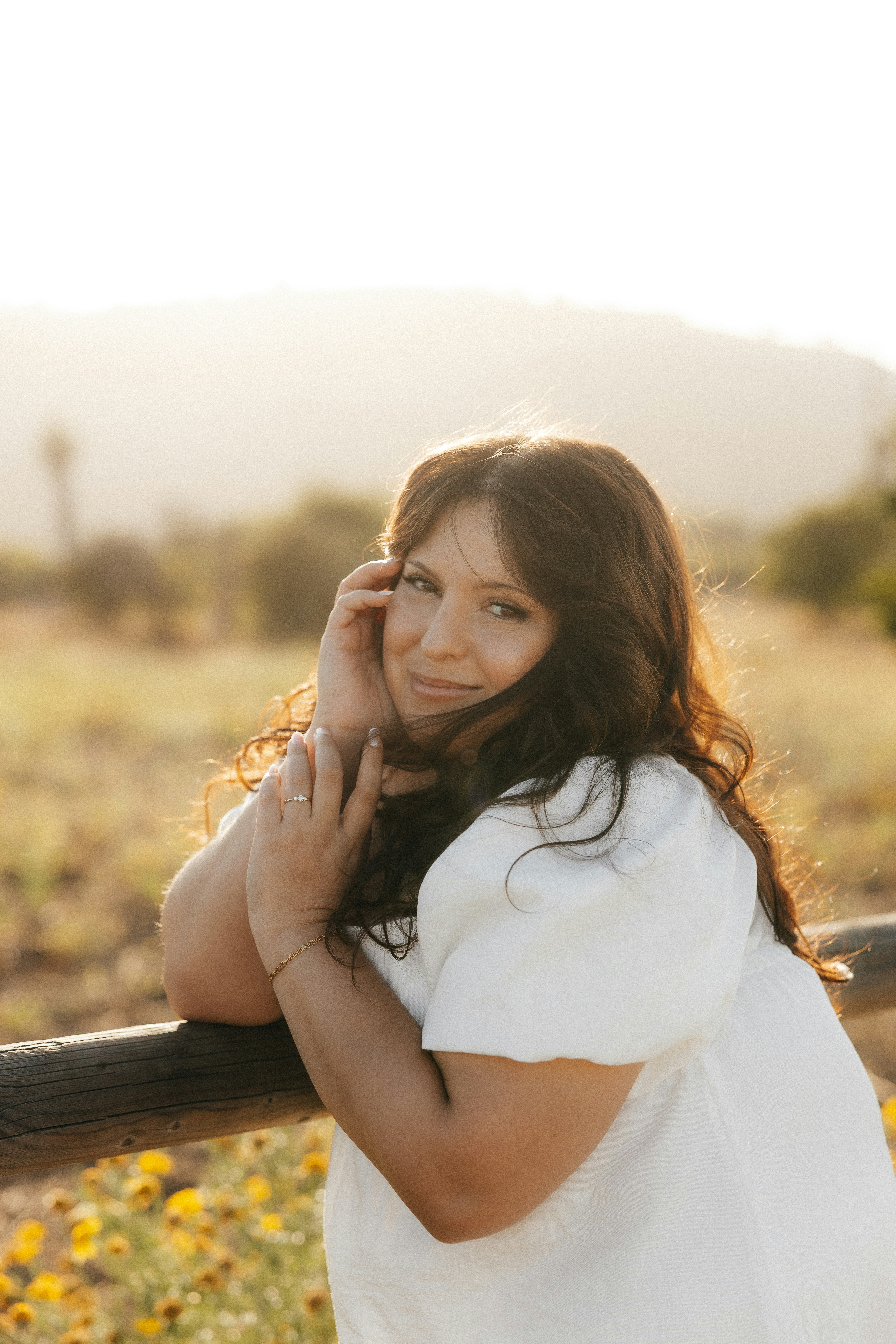 A woman rests her arm on a wooden fence outdoors.