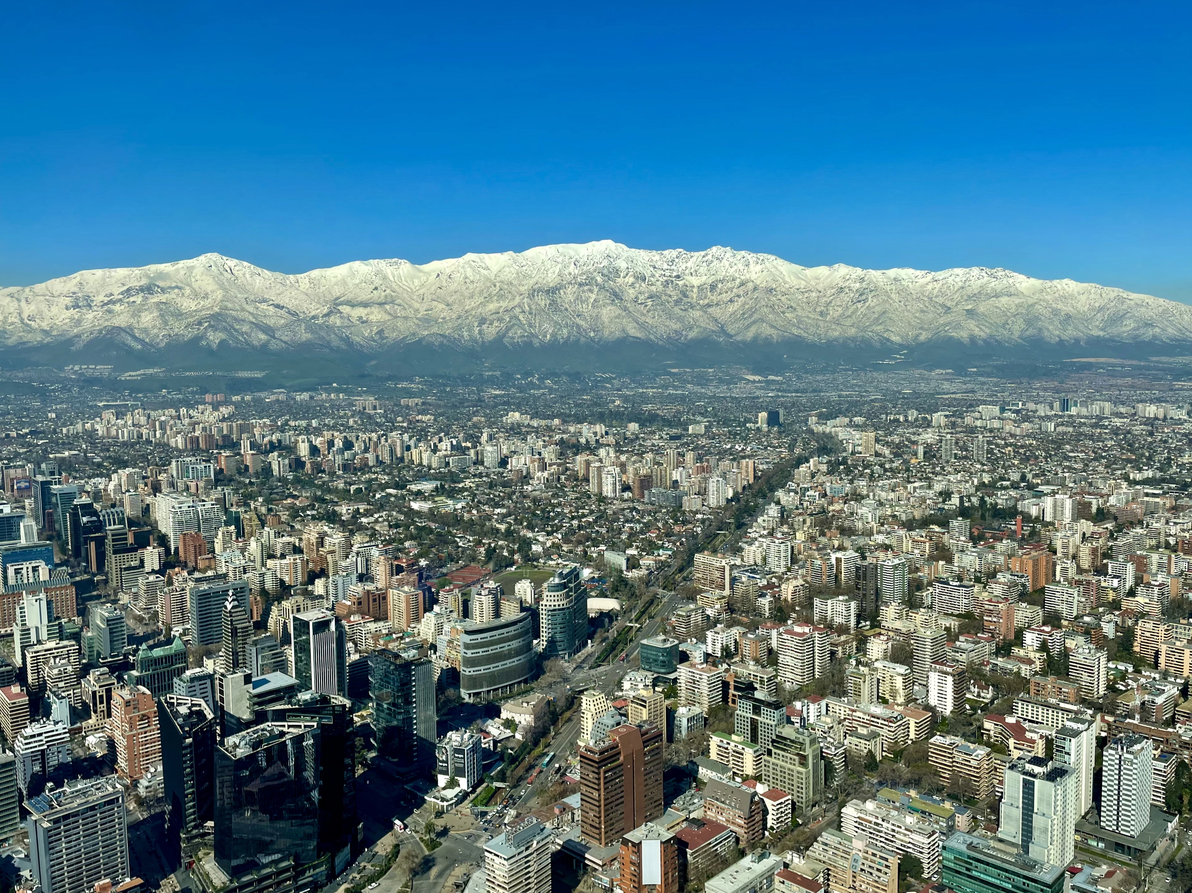 An aerial view of Santiago's dense downtown grid stretching toward a wall of snow-capped Andes peaks.