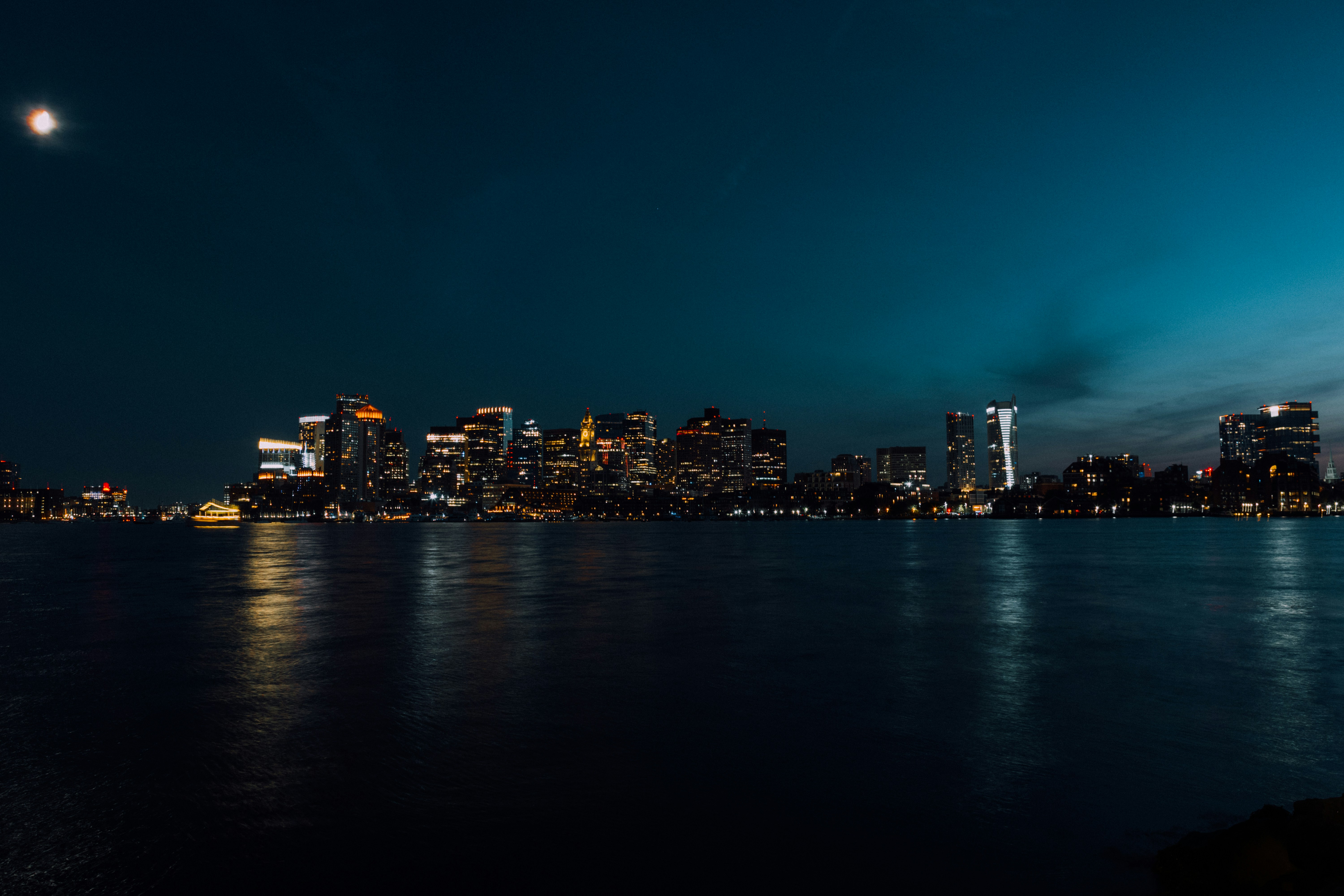 City skyline illuminated at night with moon overhead.