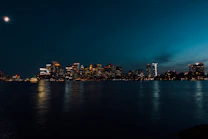 City skyline illuminated at night with moon overhead.