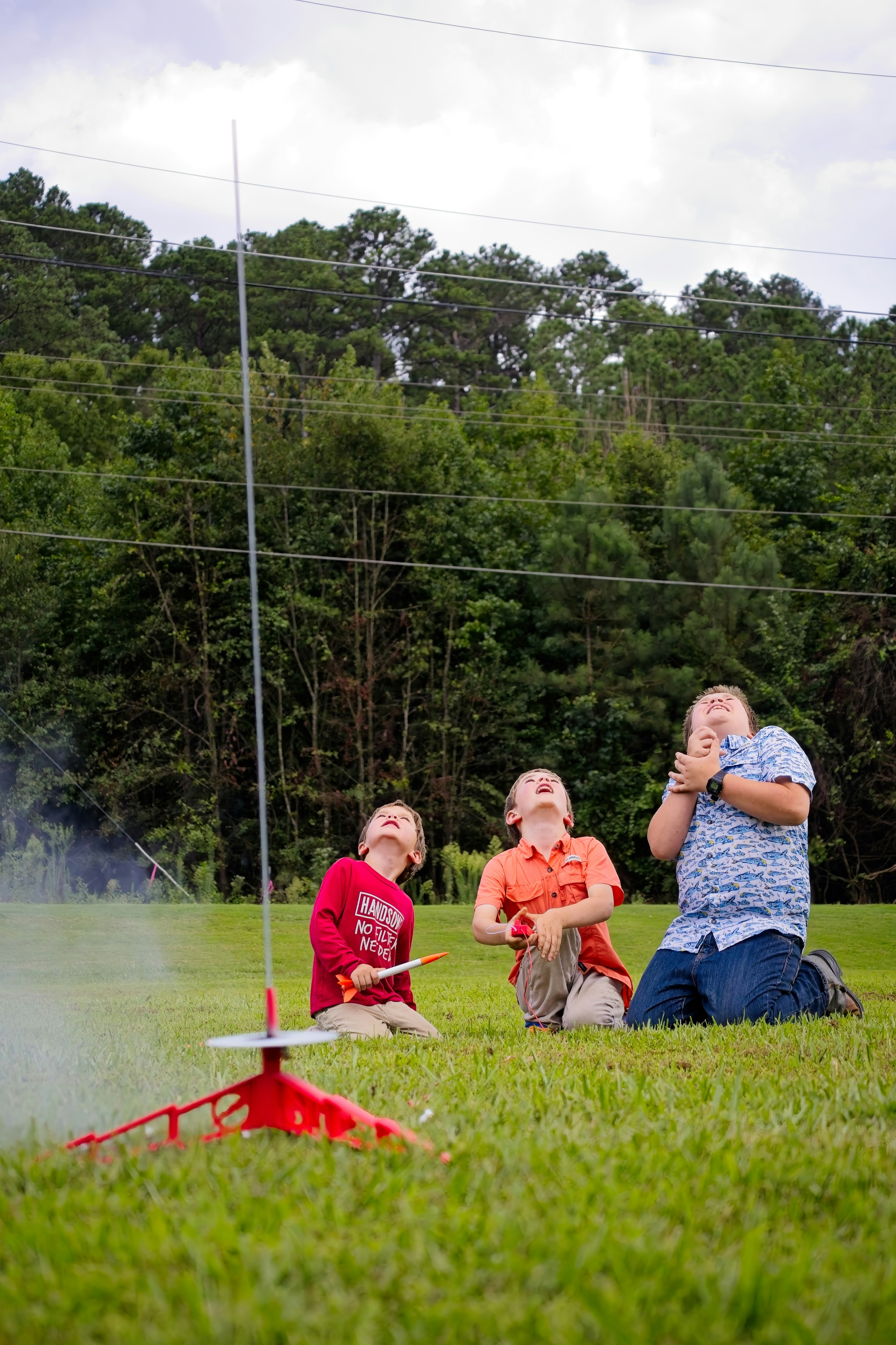 Three boys watching a rocket launch in a field