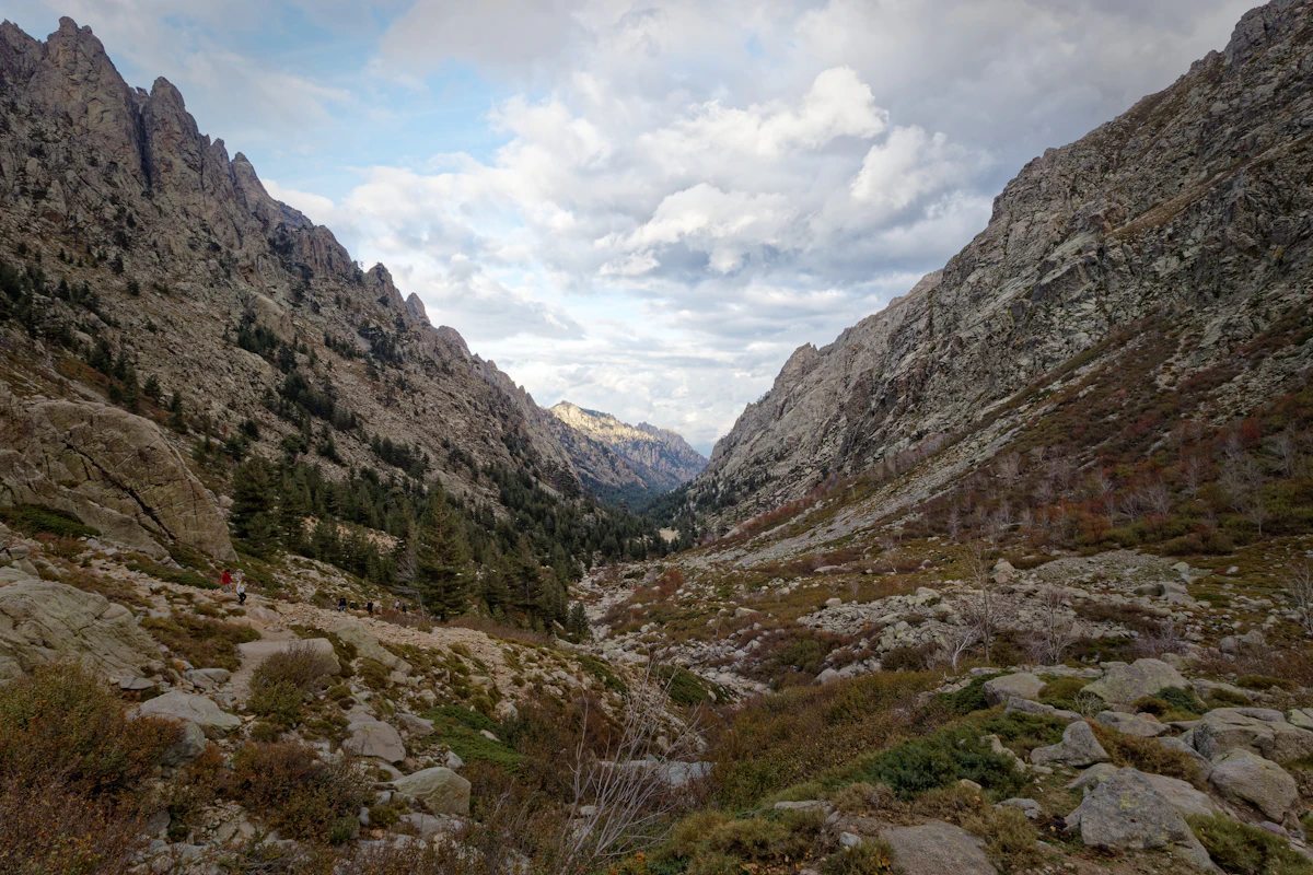 The Restonica valley near Corte, with pines and scree below jagged rocky ridges under a cloudy sky