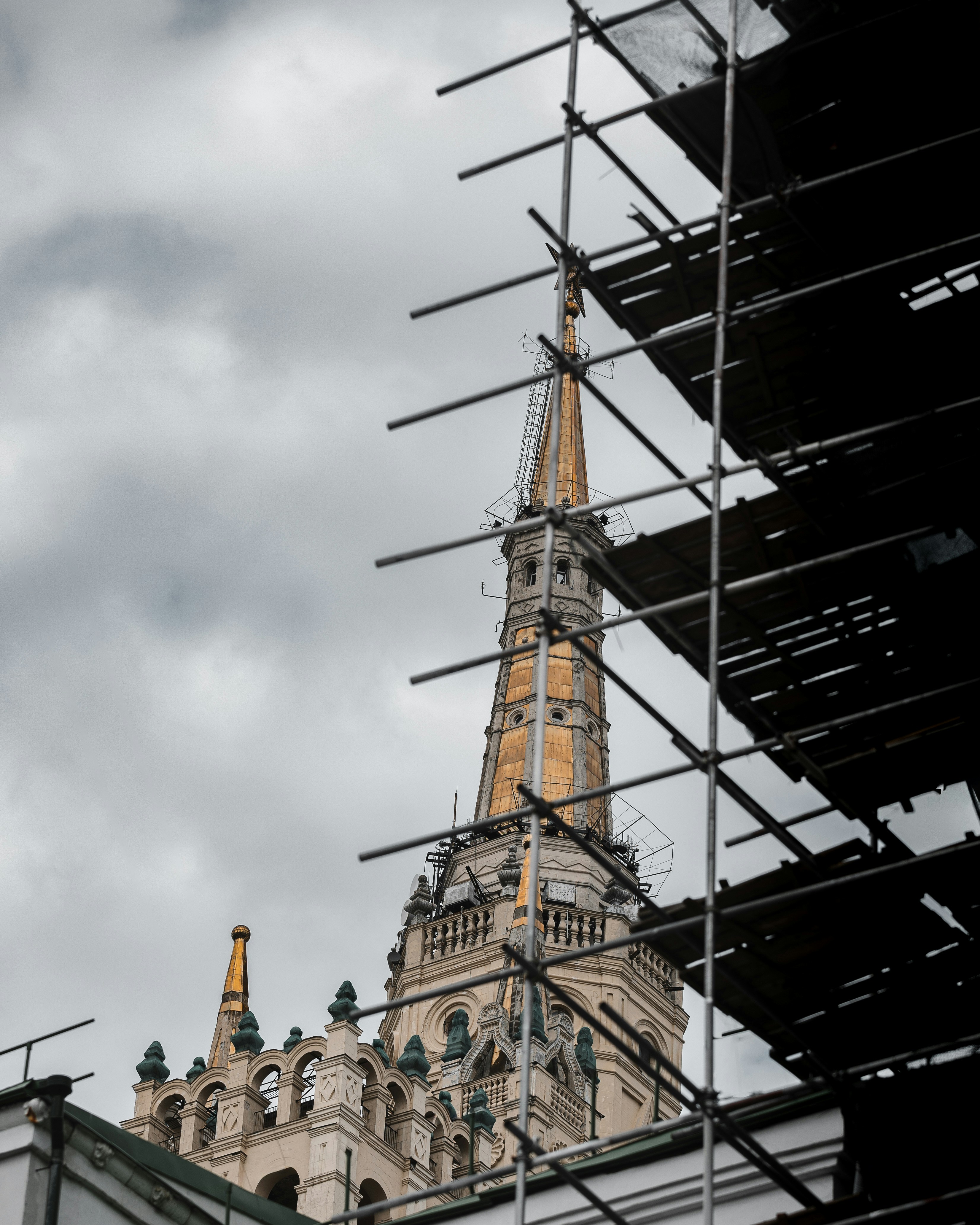 Scaffolding surrounds a tall church spire under cloudy skies.