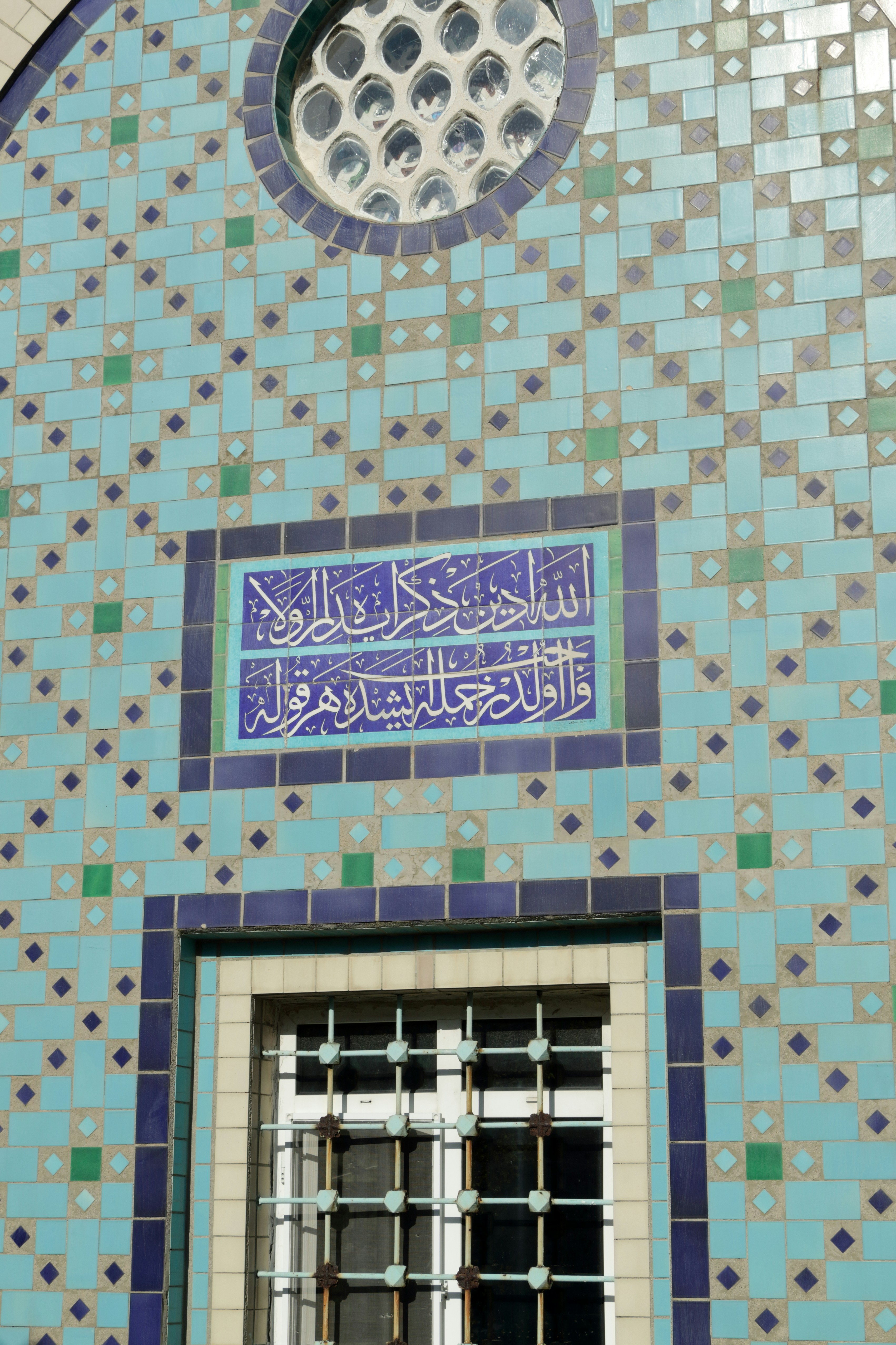 Ornate blue and green tiled building facade with arabic calligraphy.