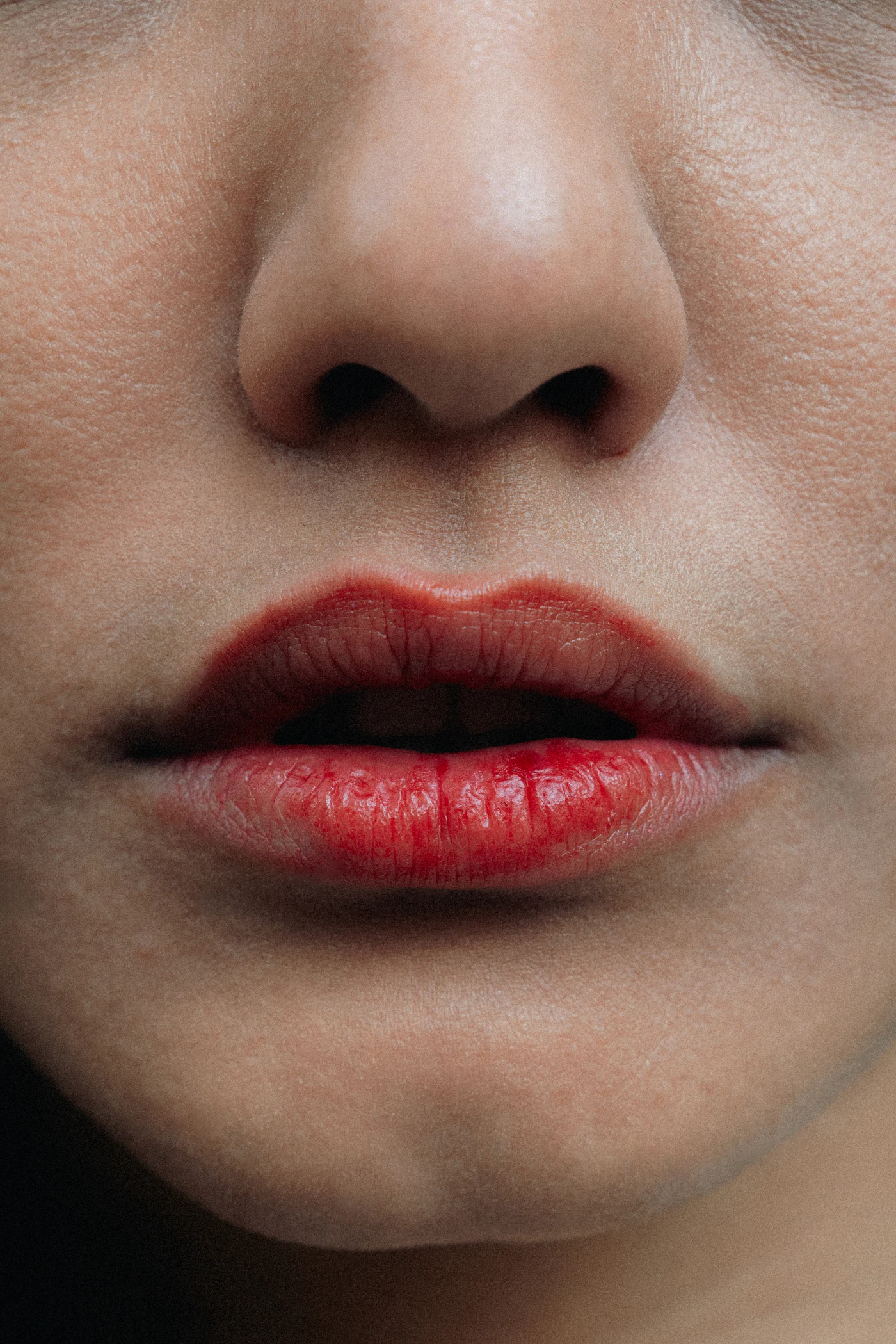 Extreme close-up of full lips with vivid red lipstick, slightly parted beneath the nose.