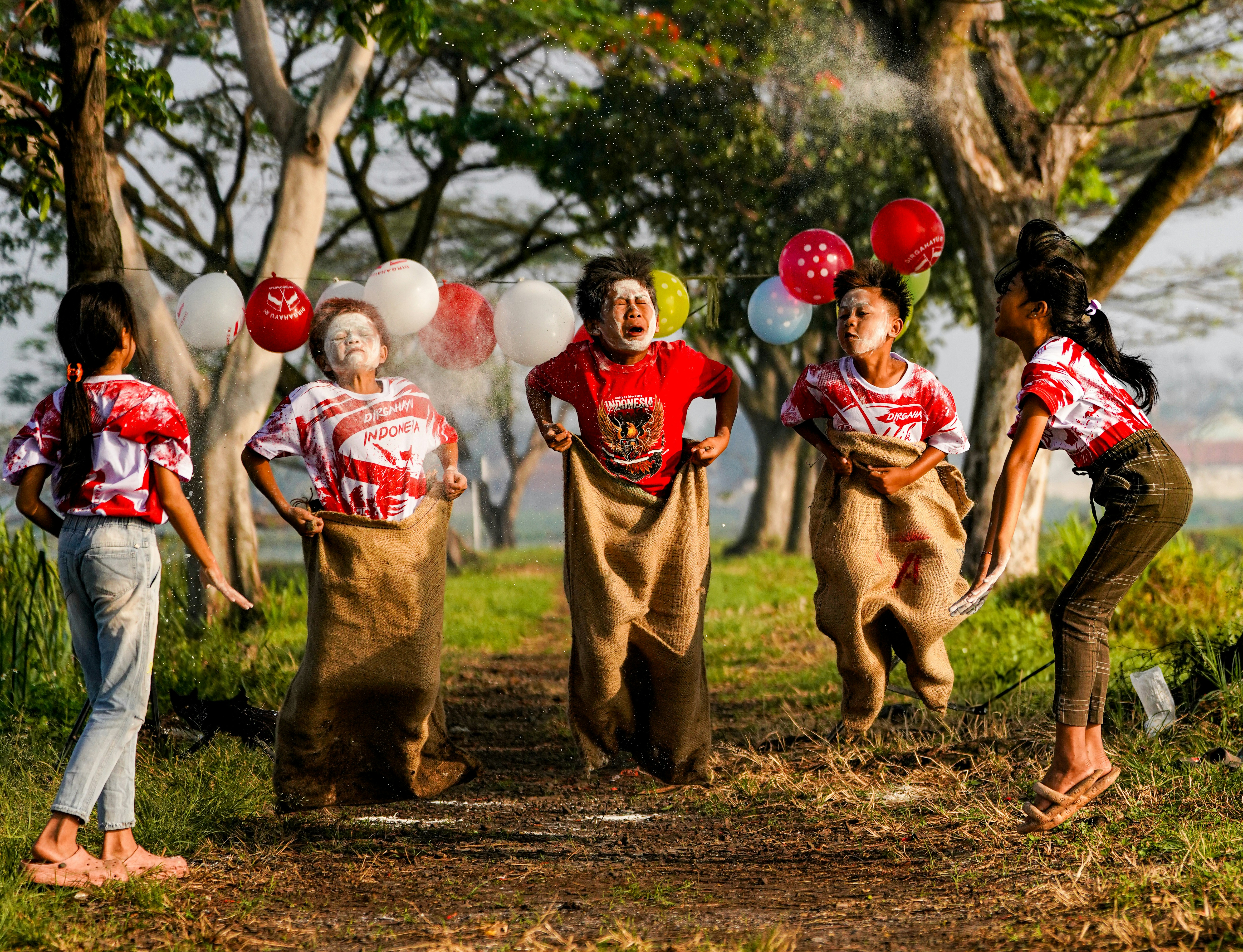 Children enjoy a sack race outdoors with balloons.