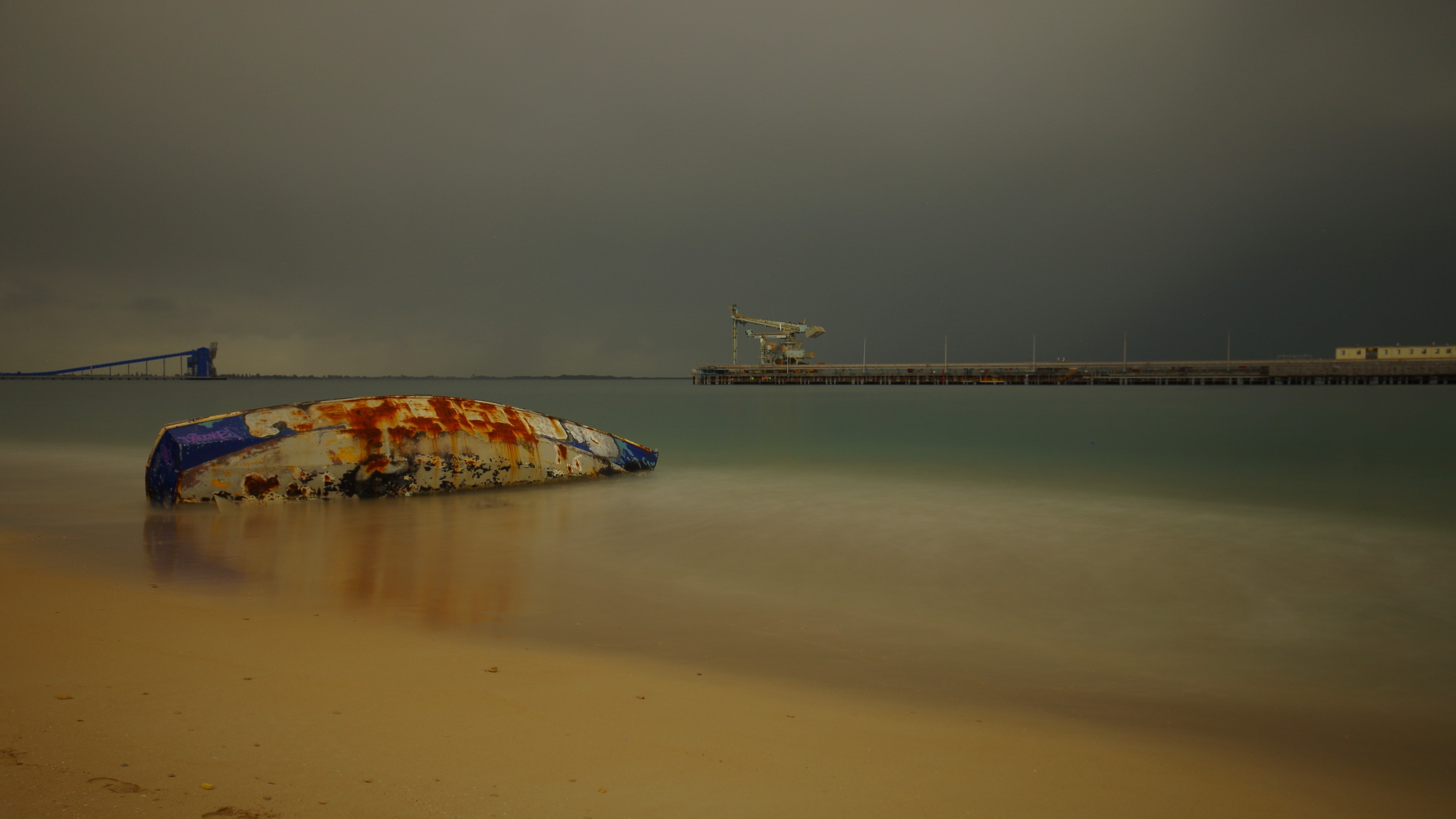 Capsized boat washed ashore on a beach with calm waters.