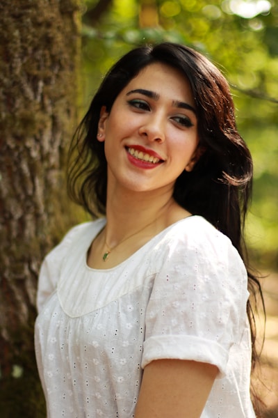 A woman smiles while leaning against a tree.