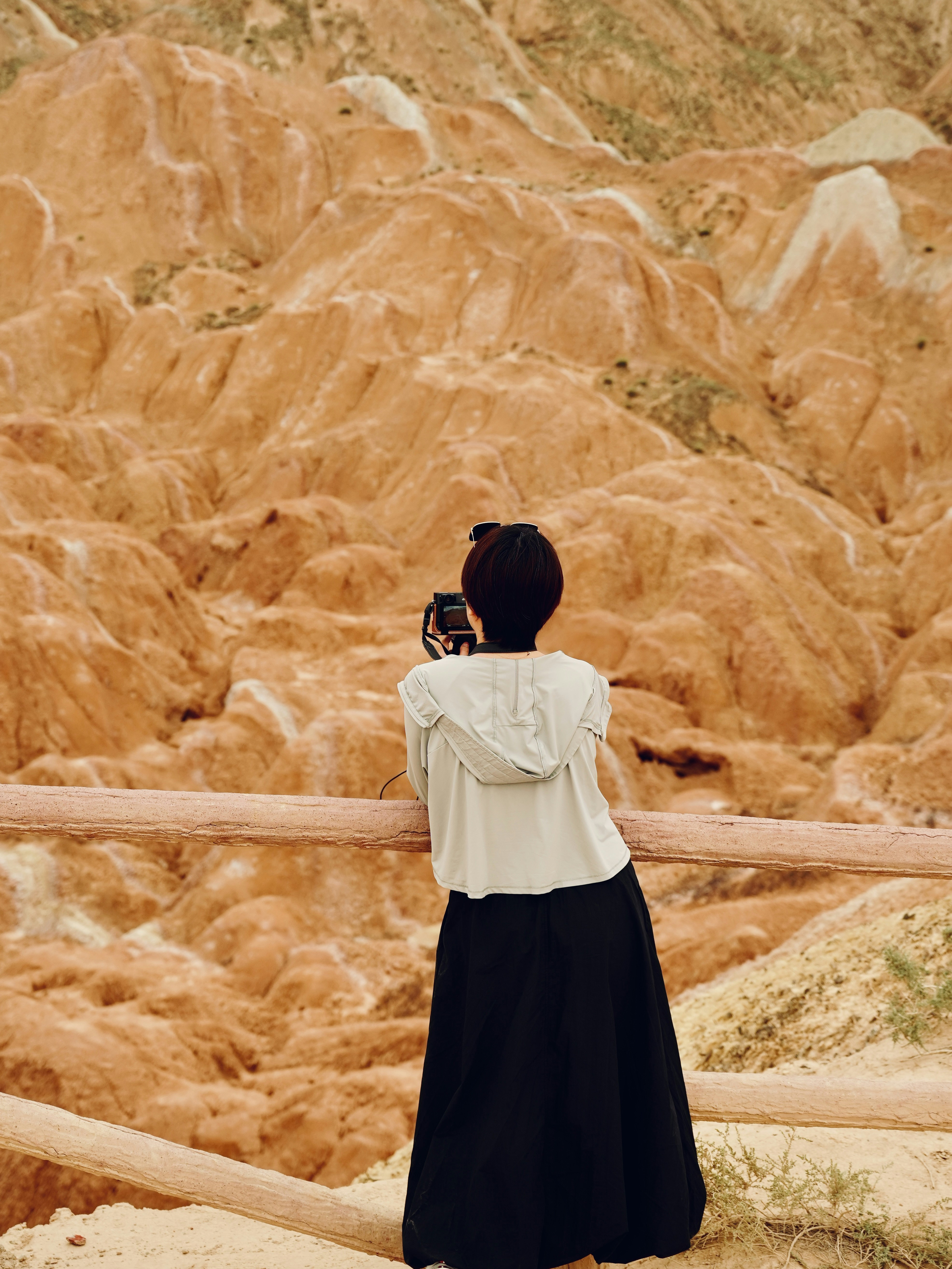 Woman photographing colorful desert landscape from wooden fence