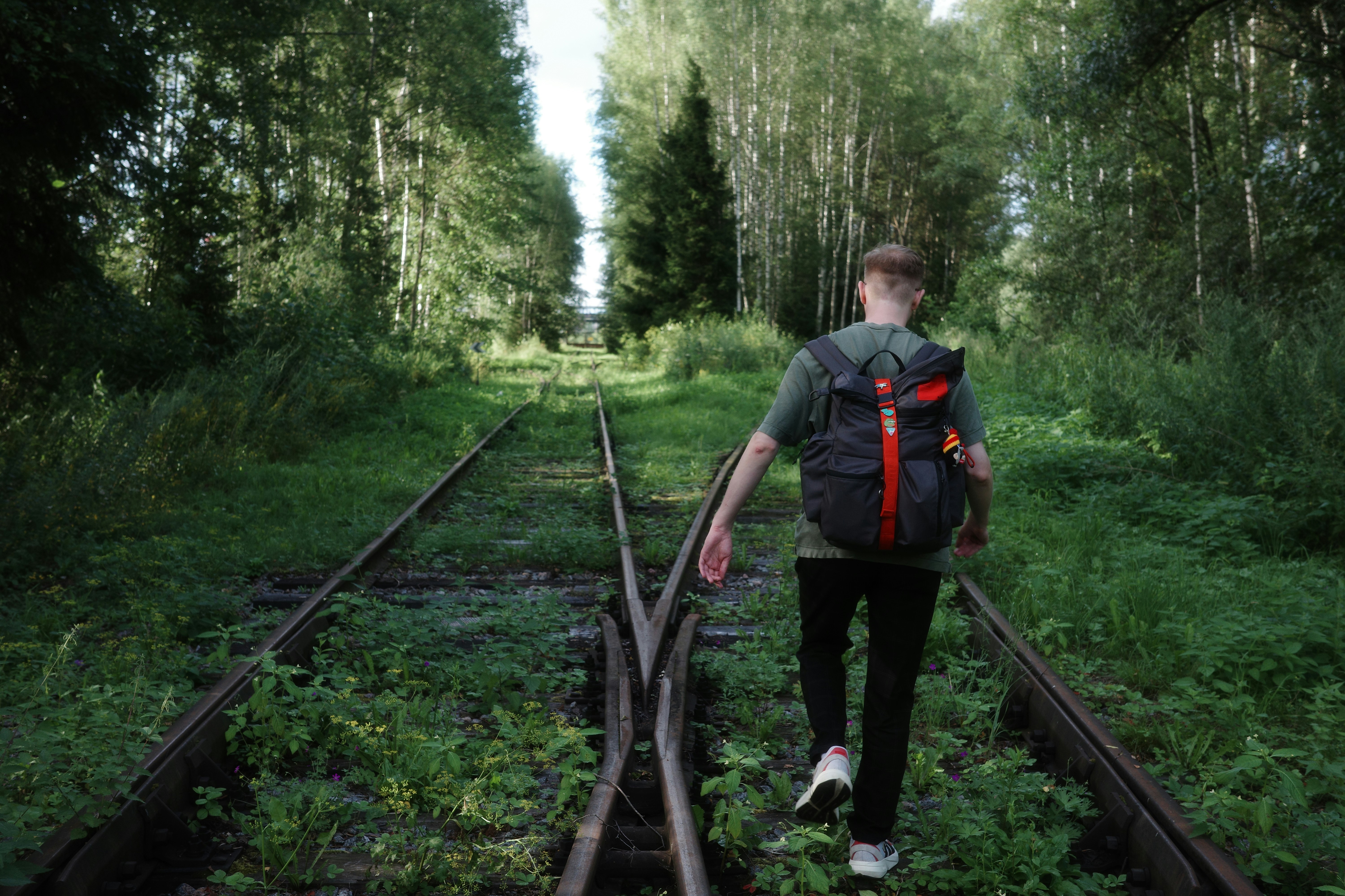 Young person walks on overgrown train tracks